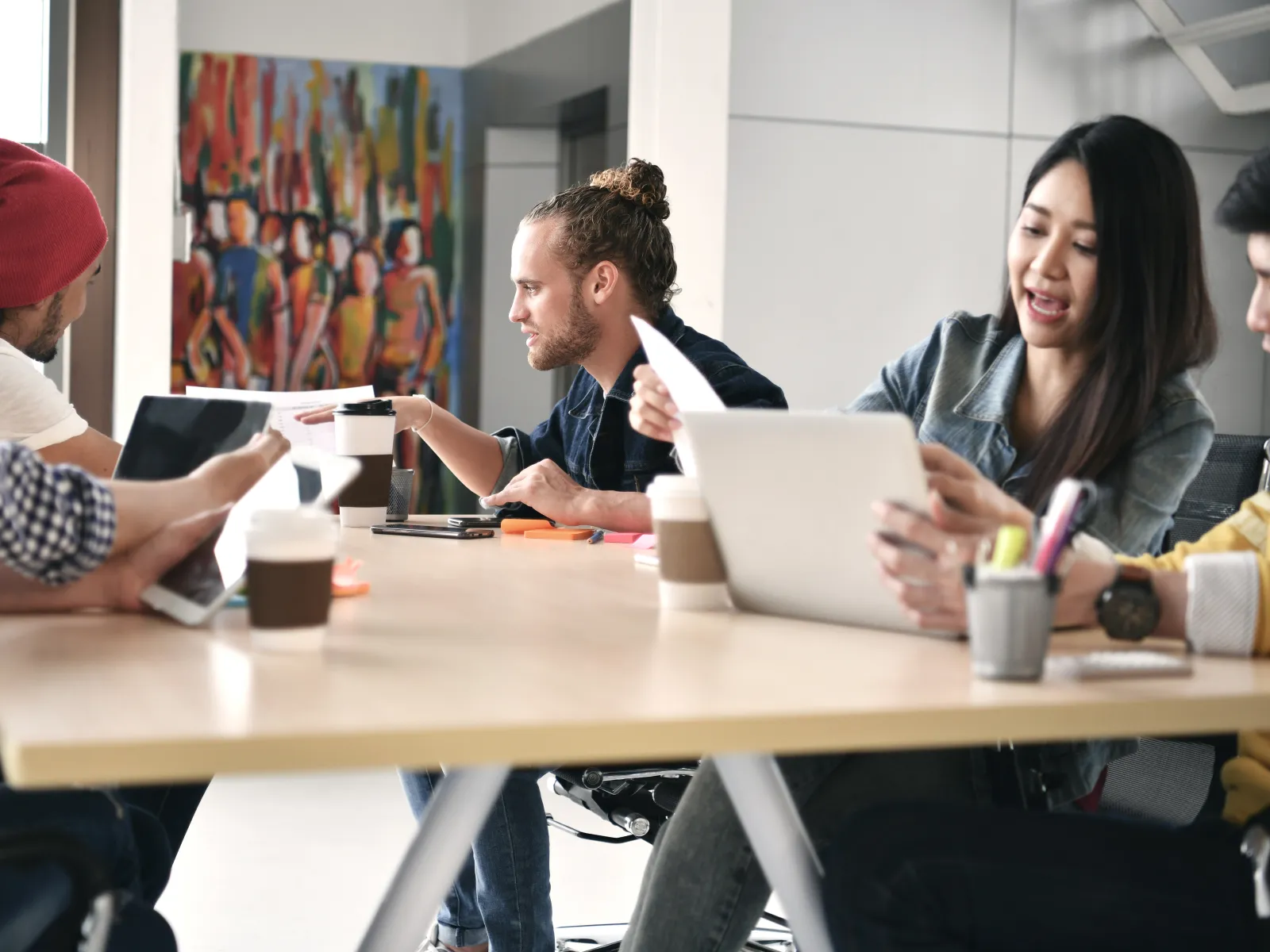 Group of diverse individuals collaborating in a modern office setting with laptops and coffee.