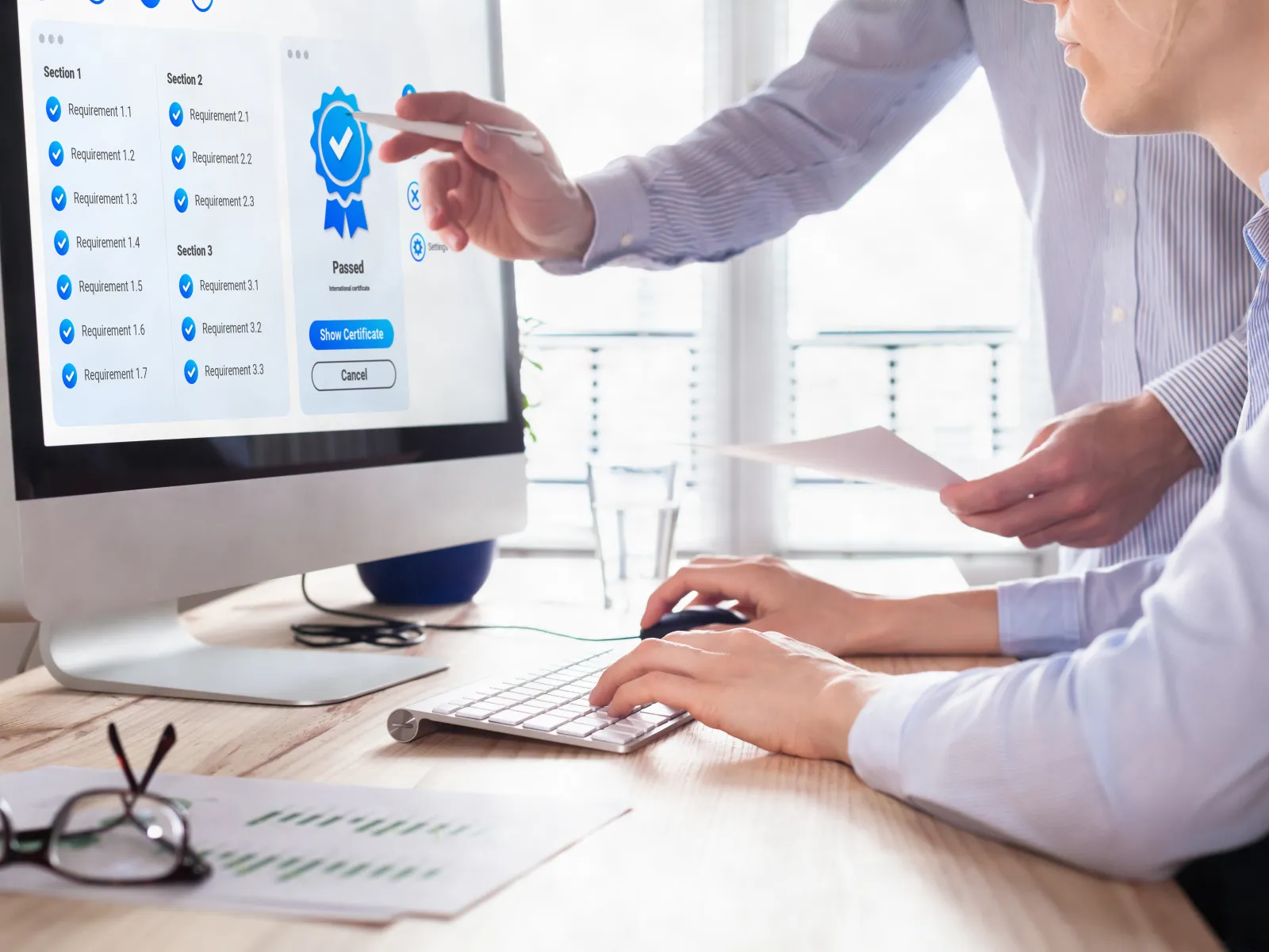 Two people reviewing a digital certification process on a computer screen in an office setting.