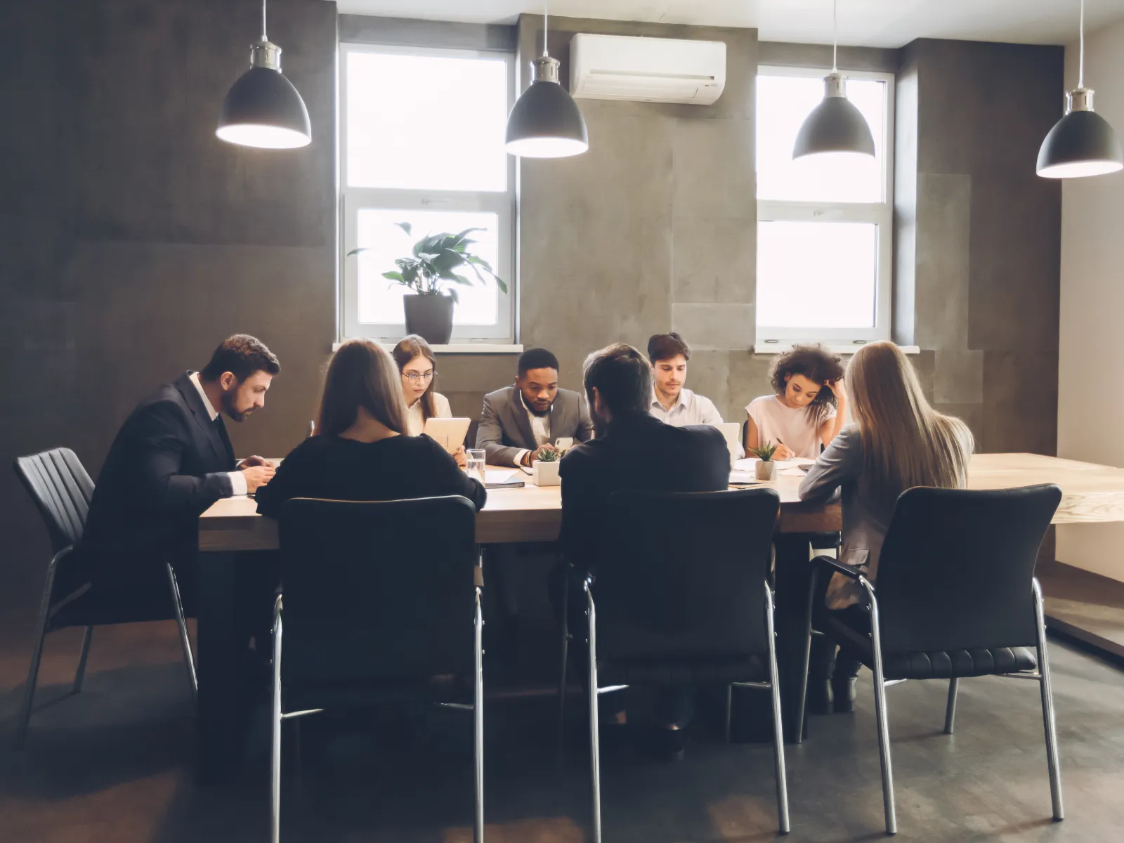 Business team having a meeting around a table in a modern office with natural light and pendant lamps.