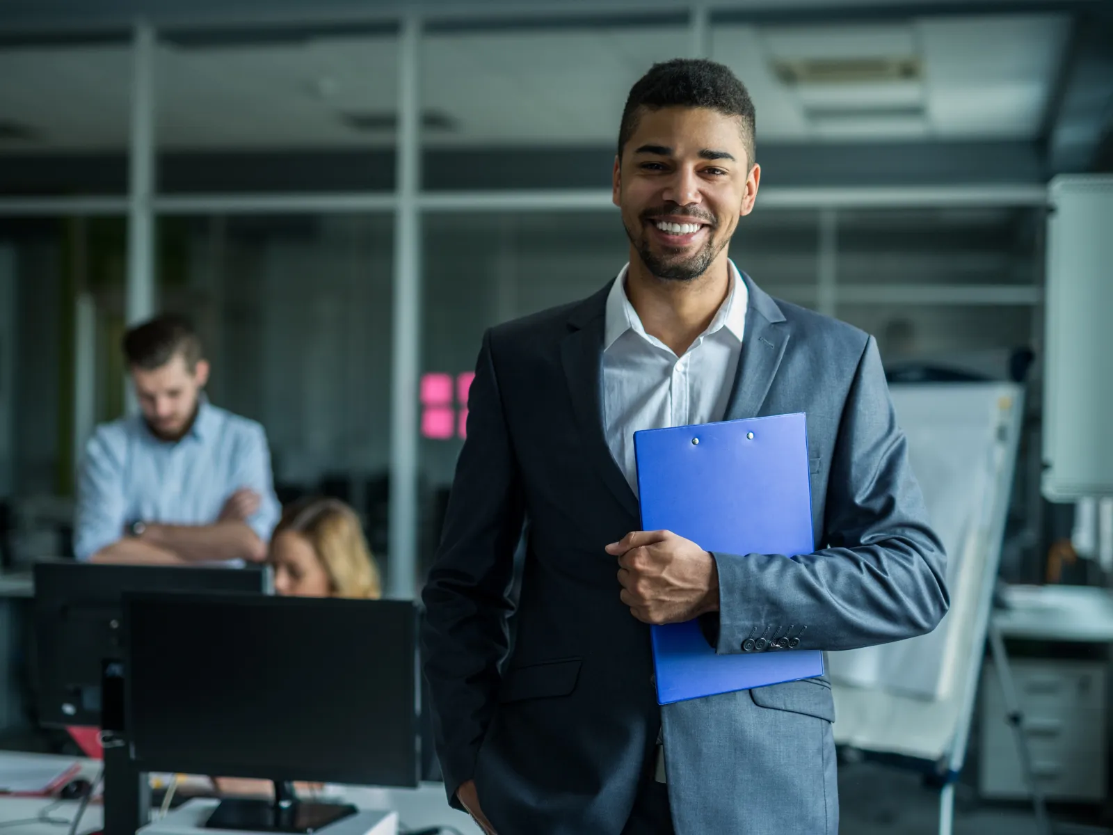 Confident businessman in a suit holding a clipboard in a modern office setting.