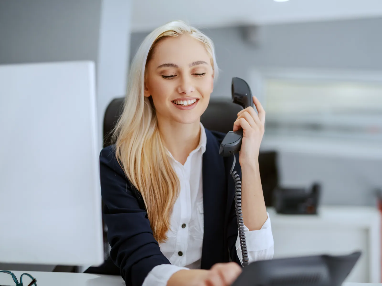 Smiling woman on a phone at her desk, engaged in a professional conversation in an office setting.