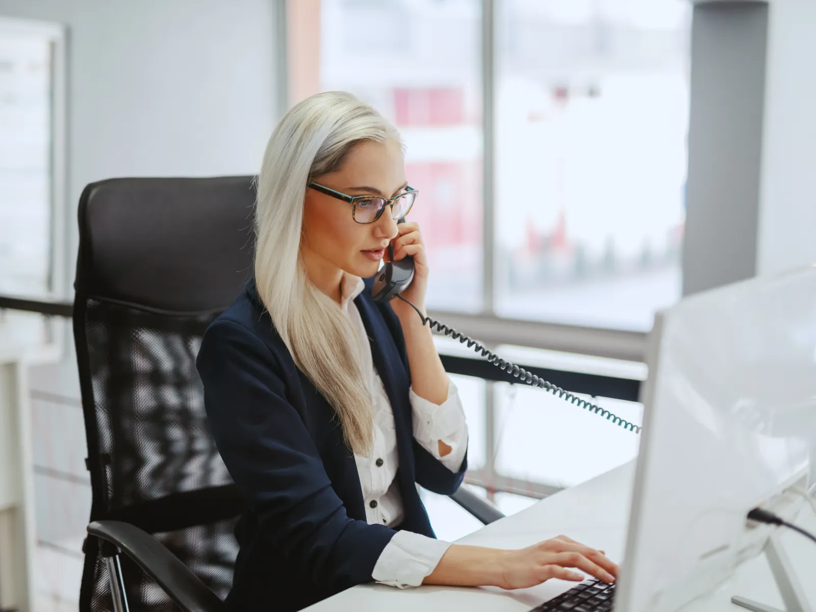 Smiling woman on a phone at her desk, engaged in a professional conversation in an office setting.