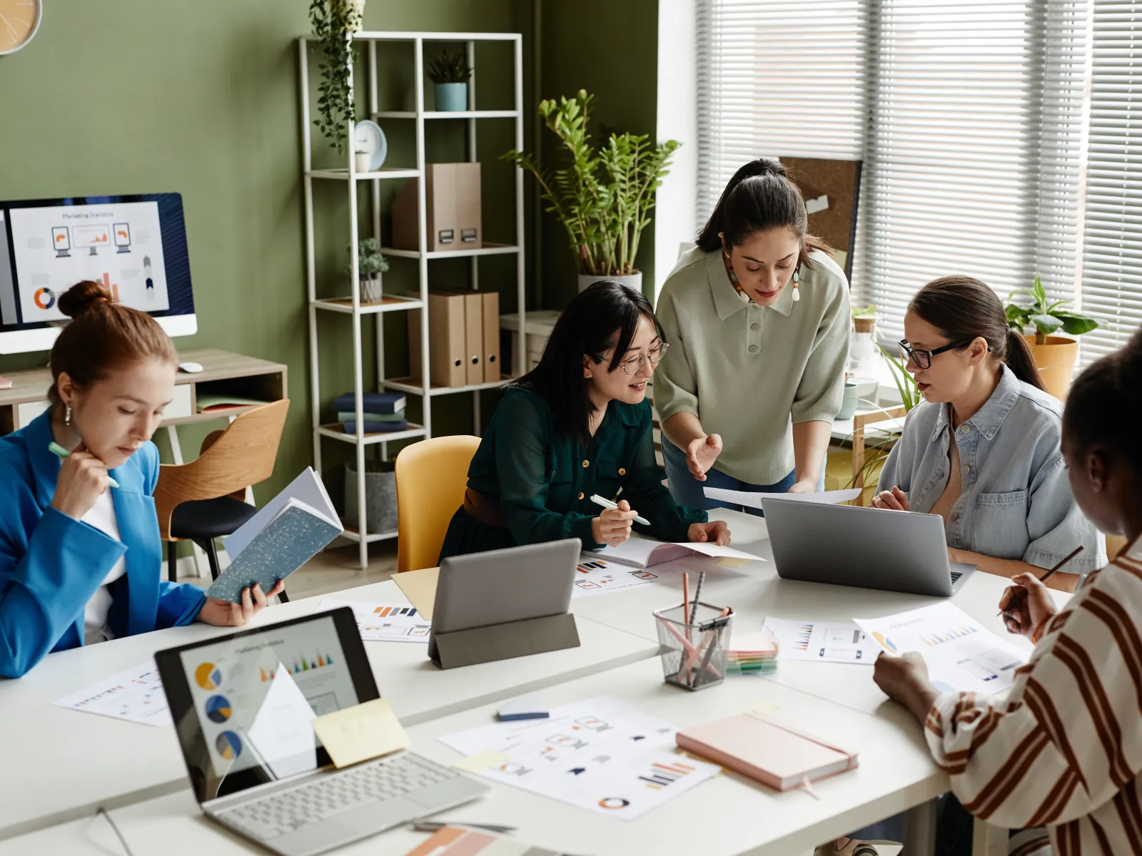 Diverse team collaborating on business project with laptops, charts, and notes in modern office setting