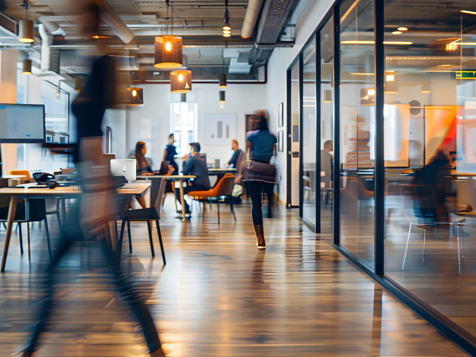 Modern office with blurred people walking and colleagues collaborating around a table in a bright workspace.