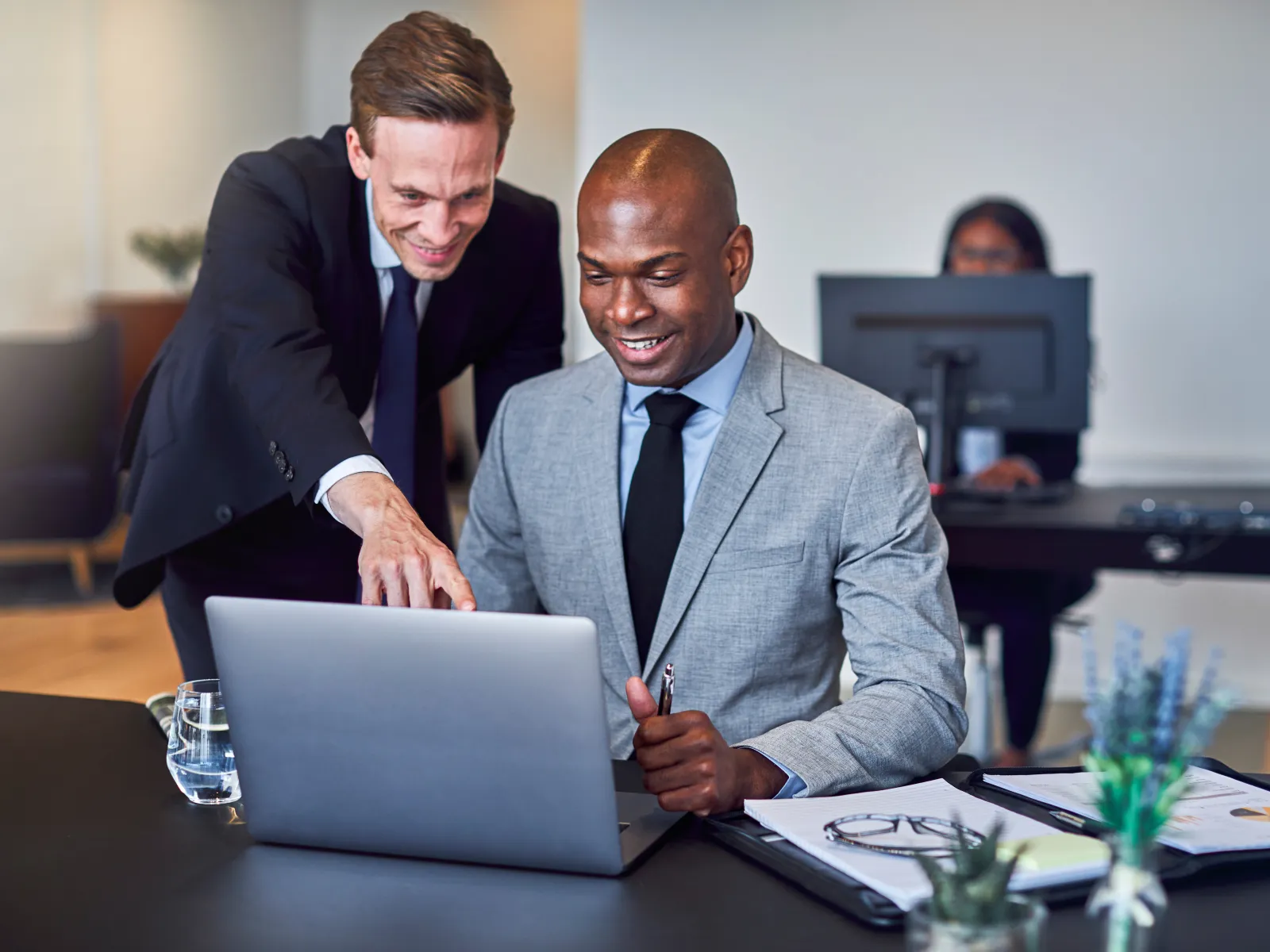 Two professionals collaborating at a laptop in a modern office setting with documents and plants.
