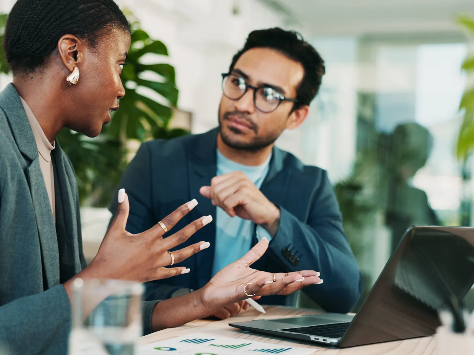 Businesswoman explaining ideas to male colleague during a meeting with laptop and charts on table