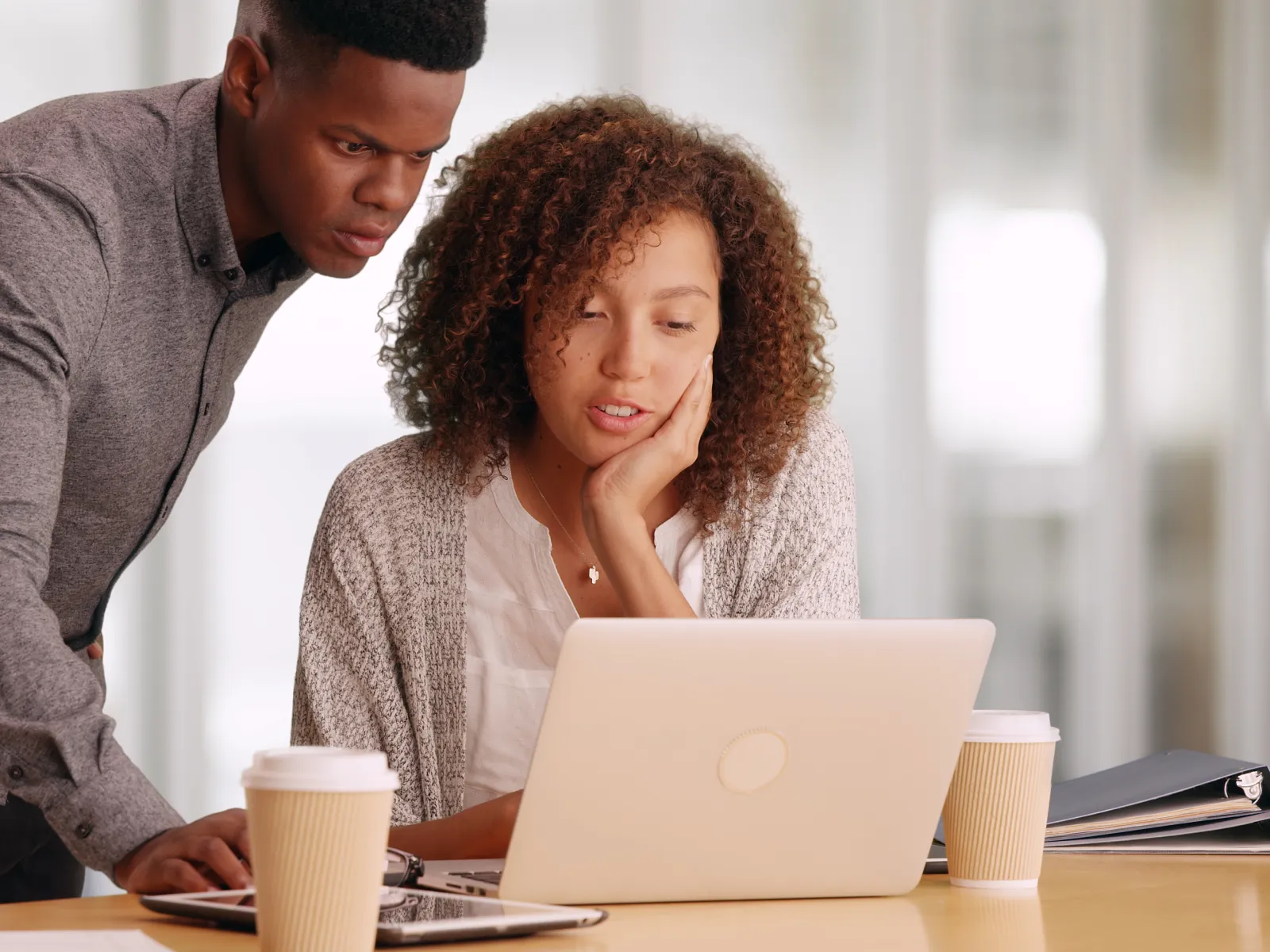 Two colleagues collaborating over a laptop in a modern workspace, coffee cups in view.