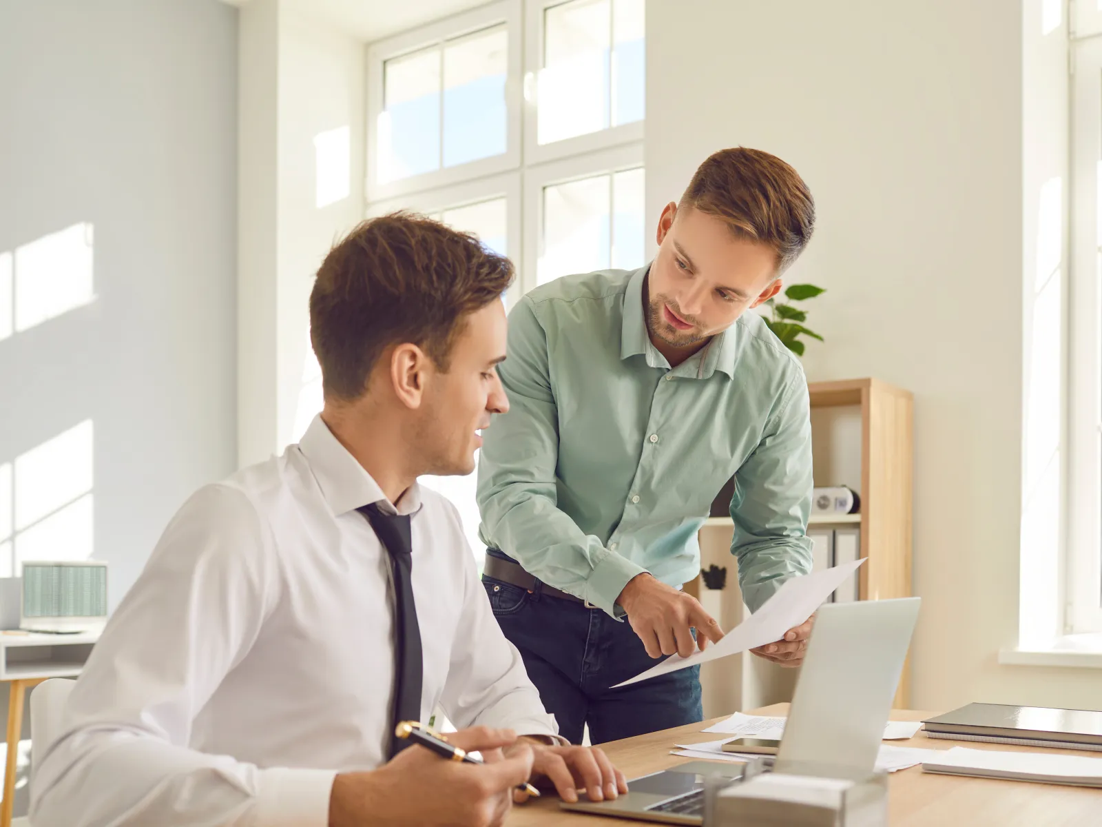 Two professionals discussing documents in a bright, modern office space with natural light.