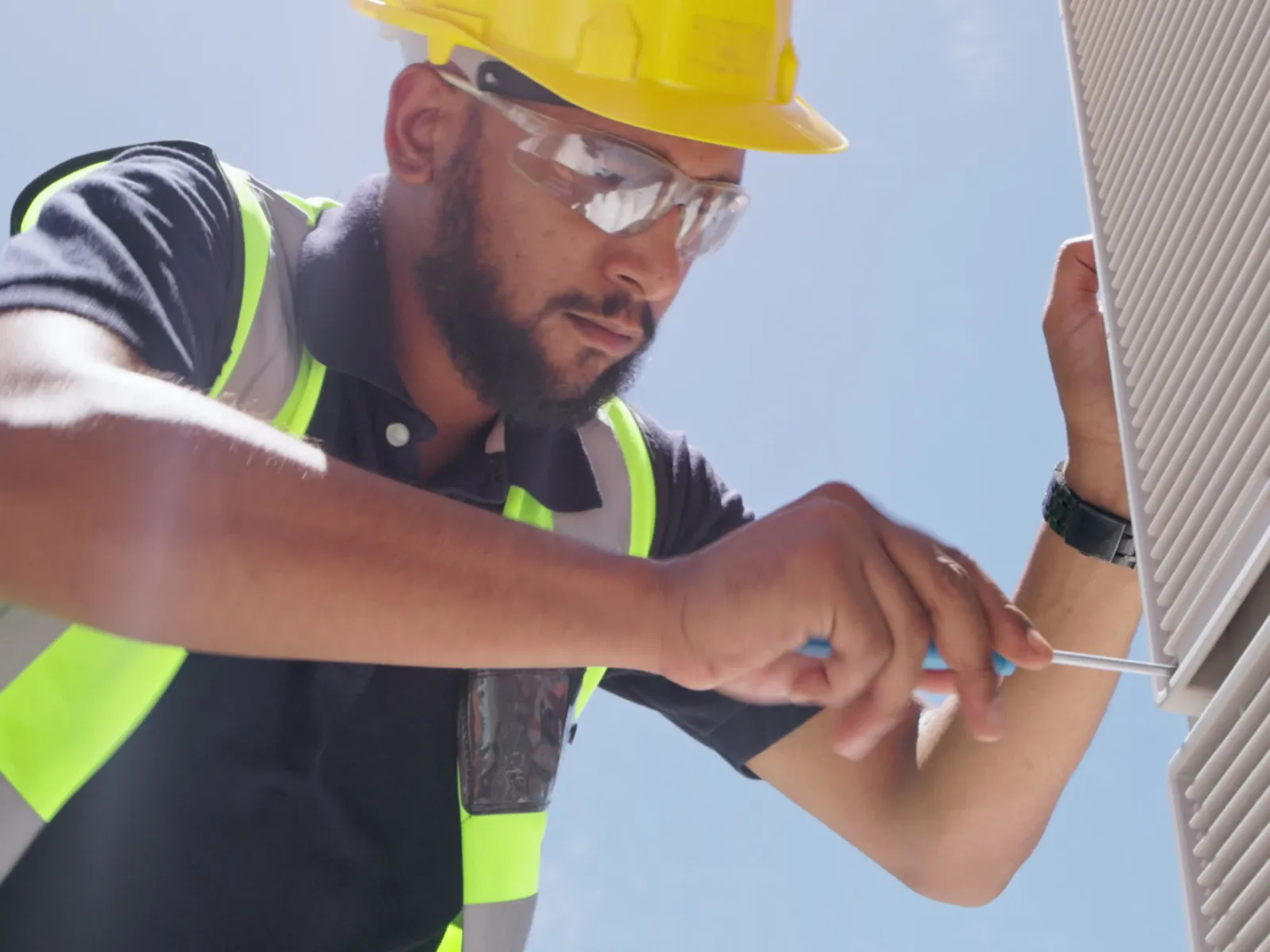 Construction worker in a hard hat and safety gear servicing a building exterior on a sunny day.
