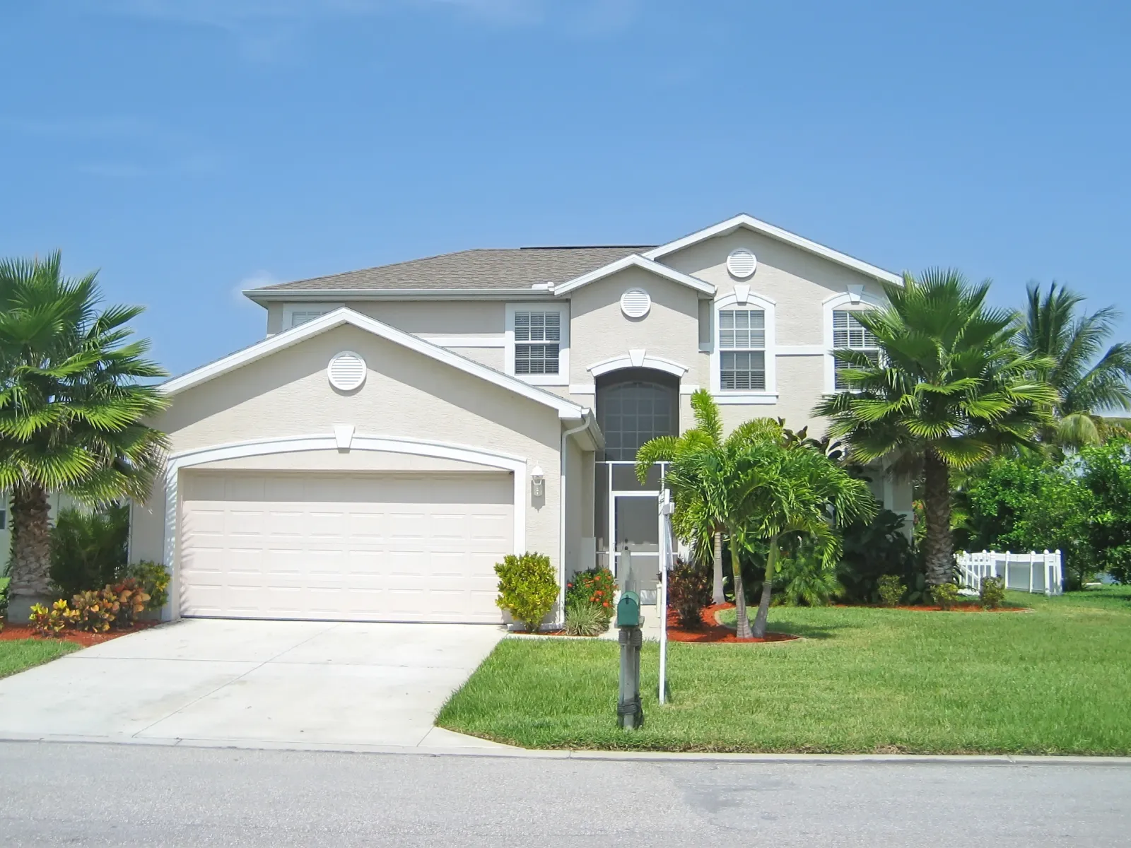 Modern two-story house with palm trees and well-maintained lawn under a clear blue sky.