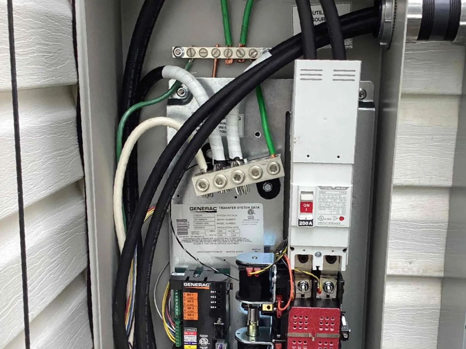 Open electrical panel with wiring, circuit breakers, and transfer switch components inside a gray metal box.