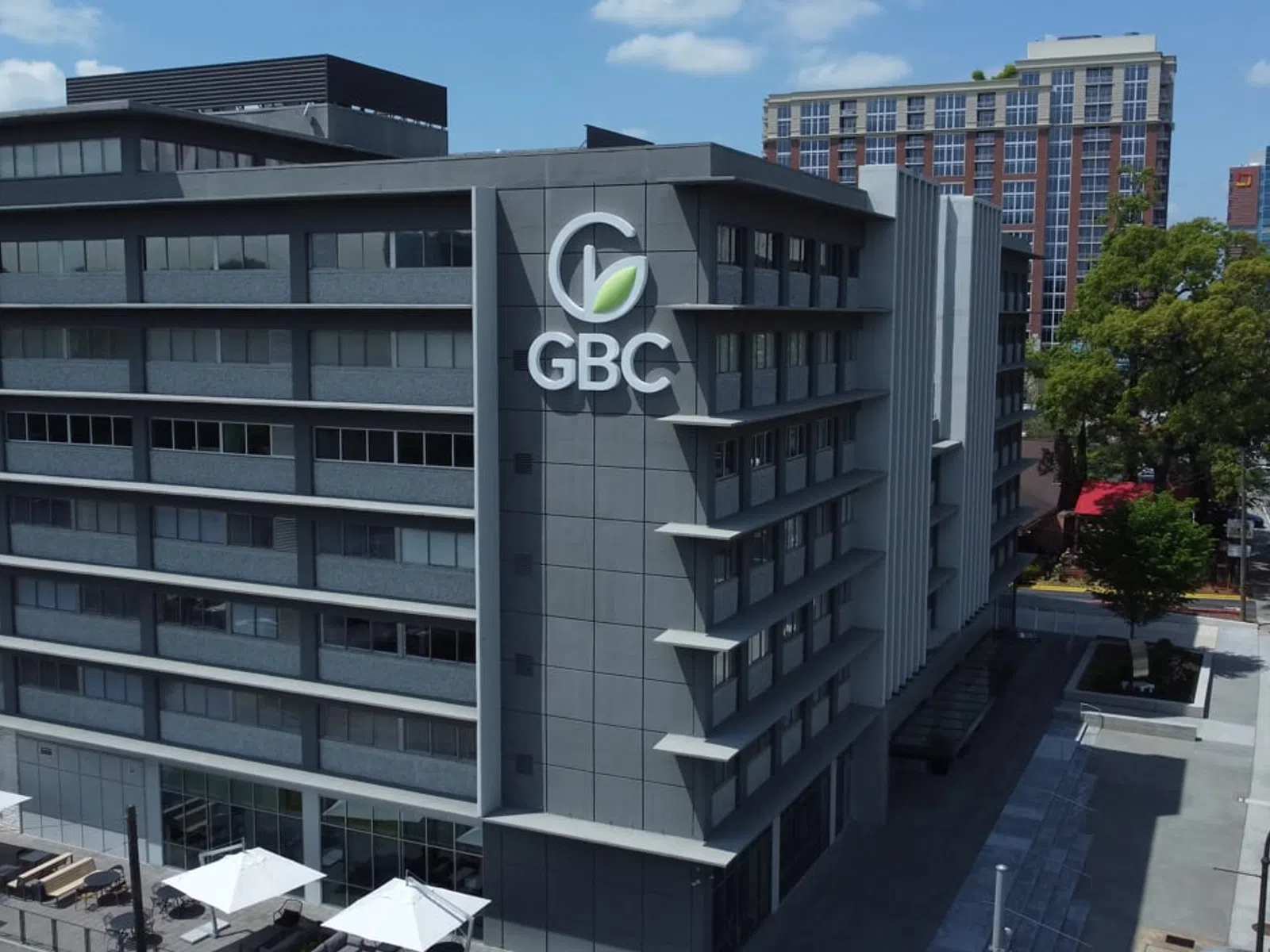 Modern multi-story office building with GBC logo on the side and cityscape in the background under clear sky.