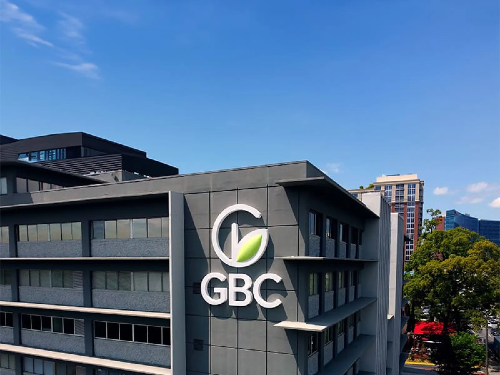 Modern office building with GBC logo featuring a green leaf under clear blue sky in urban area.