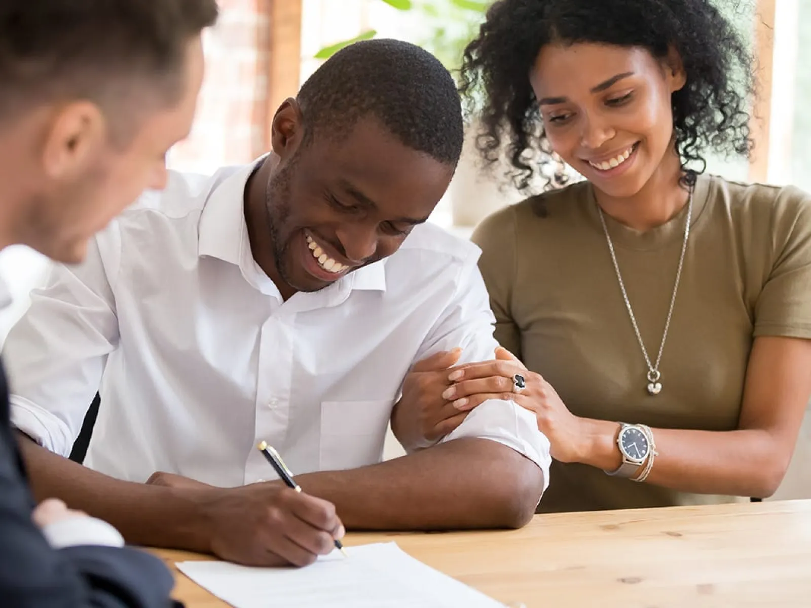 Happy couple signing a contract with business professional at a wooden table in a bright office space.