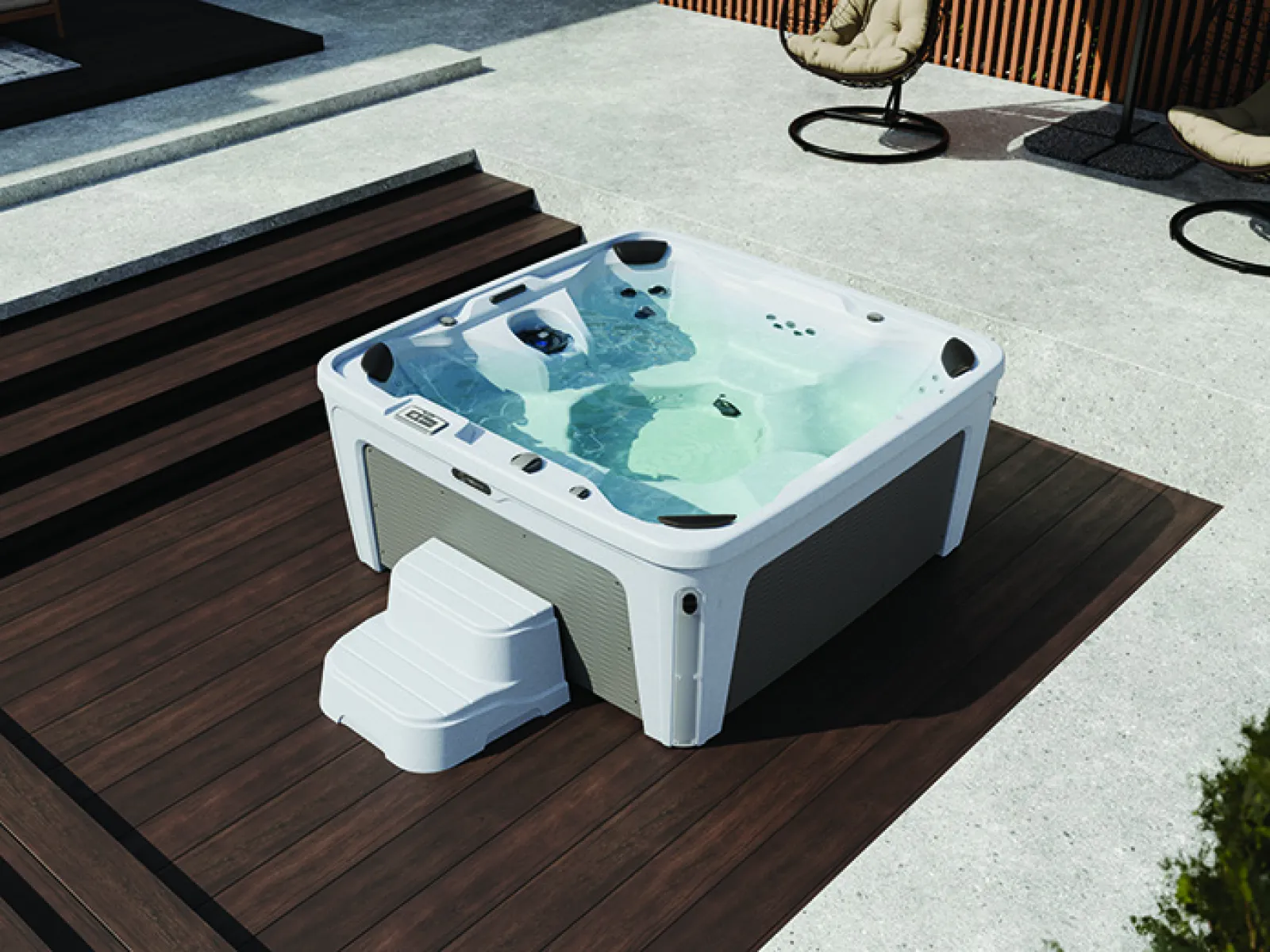 Modern outdoor hot tub with clear water on dark wooden deck surrounded by patio seating under bright daylight.