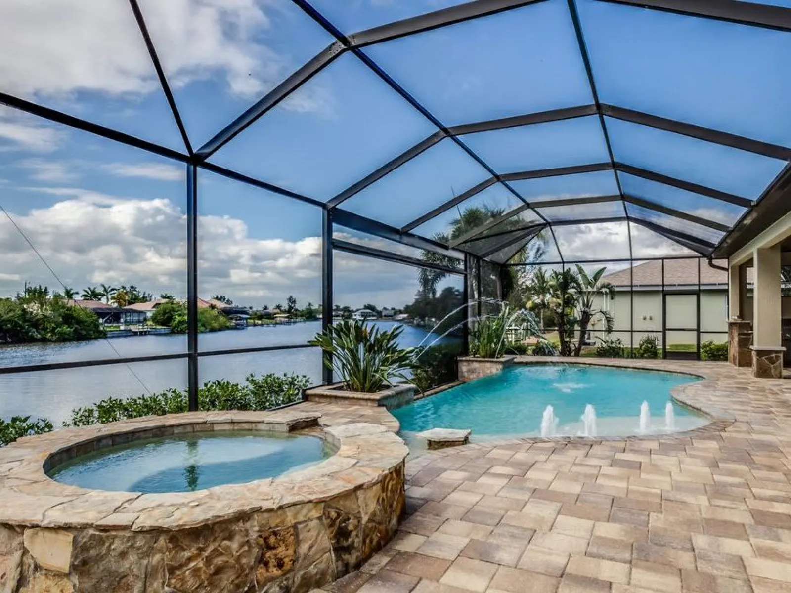 Inviting outdoor pool area with spa and water features, surrounded by lush greenery and a serene water view.