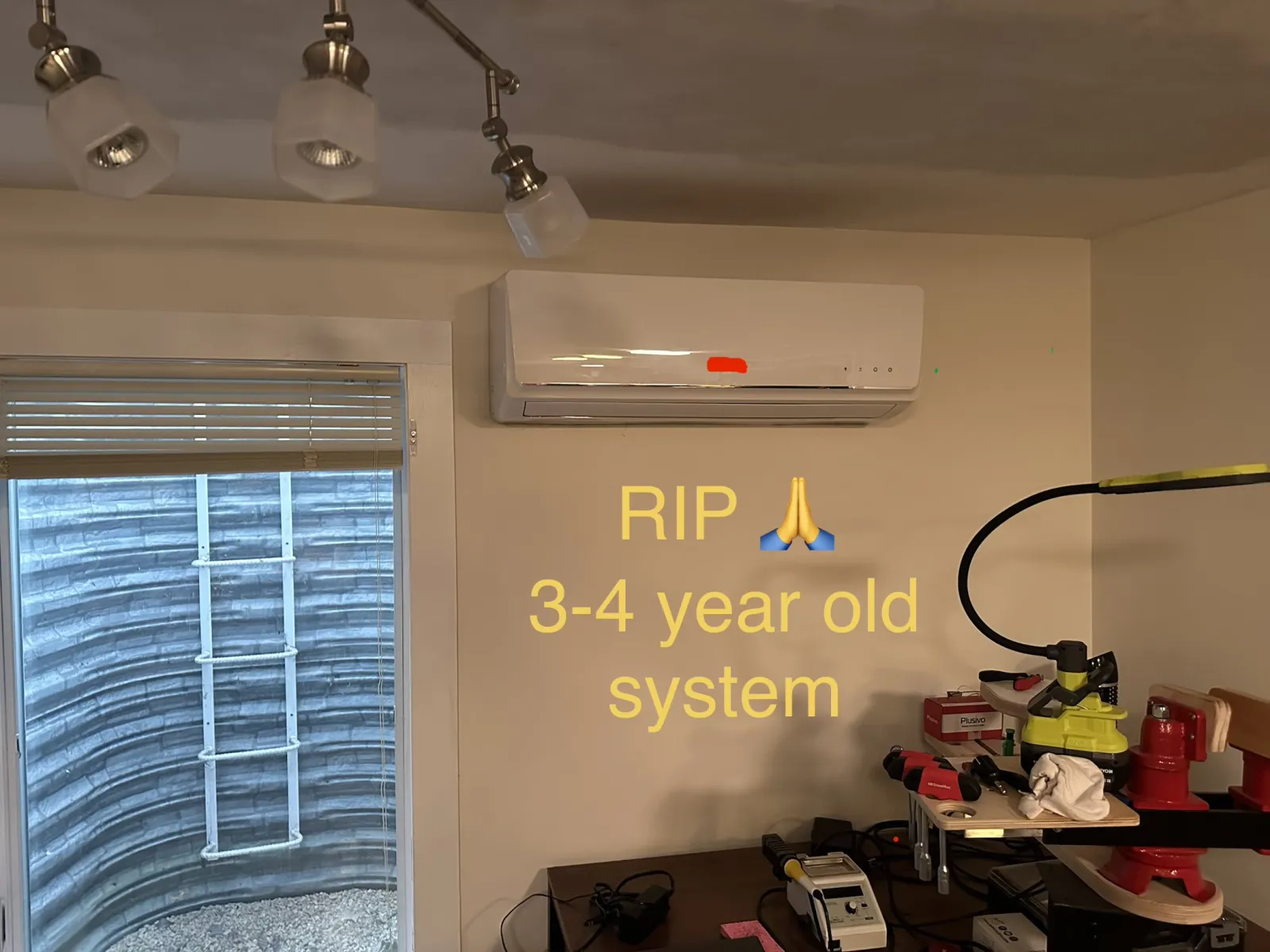 Indoor room with a wall-mounted air conditioning unit and text about a 3-4 year old system above a workbench.