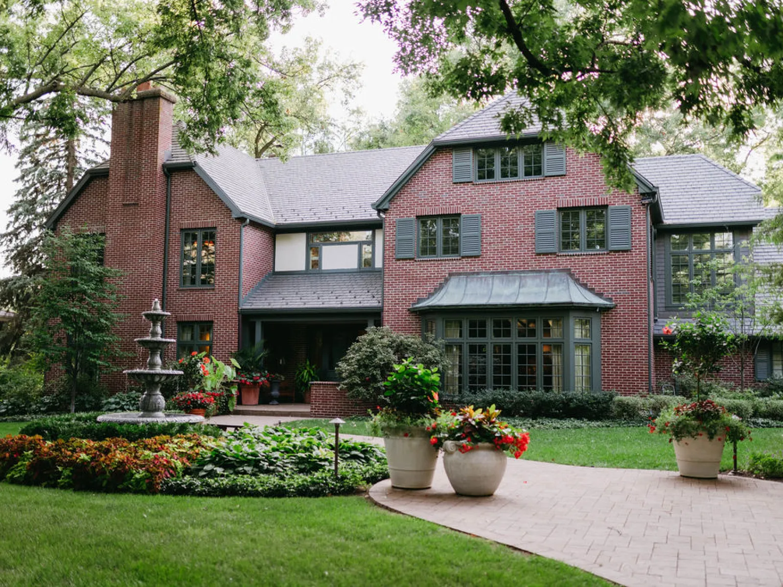 Large red brick house with multiple windows, a chimney, well-maintained garden, and a stone pathway with potted plants.