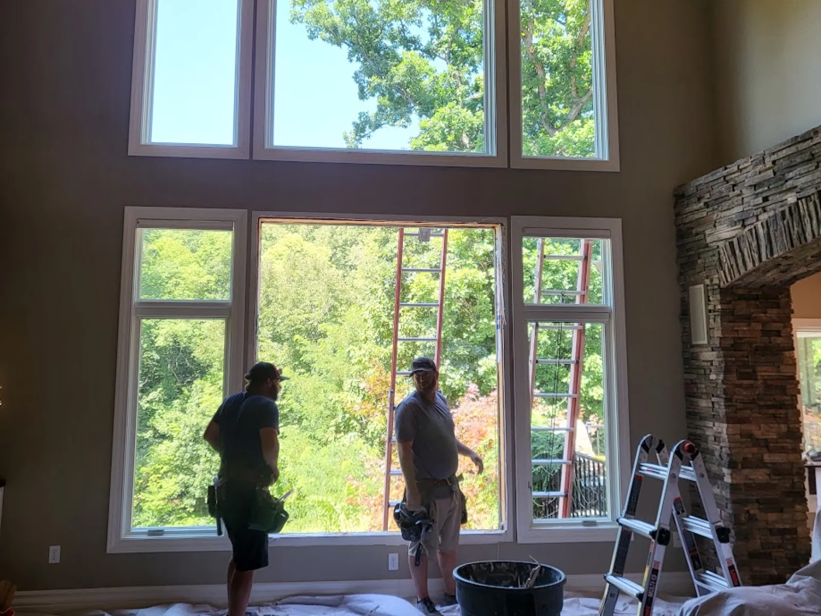 Two workers installing large windows in a modern living room with high ceilings.
