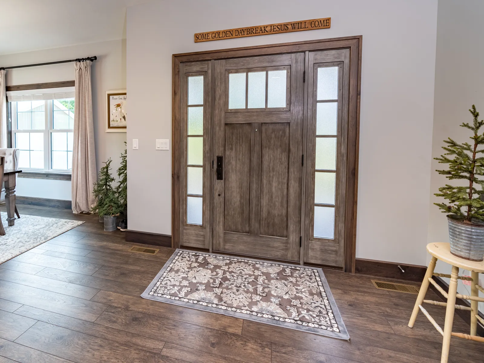 Cozy home entry with wooden front door, decorative rug, hardwood floor, plants, and dining area with natural light.