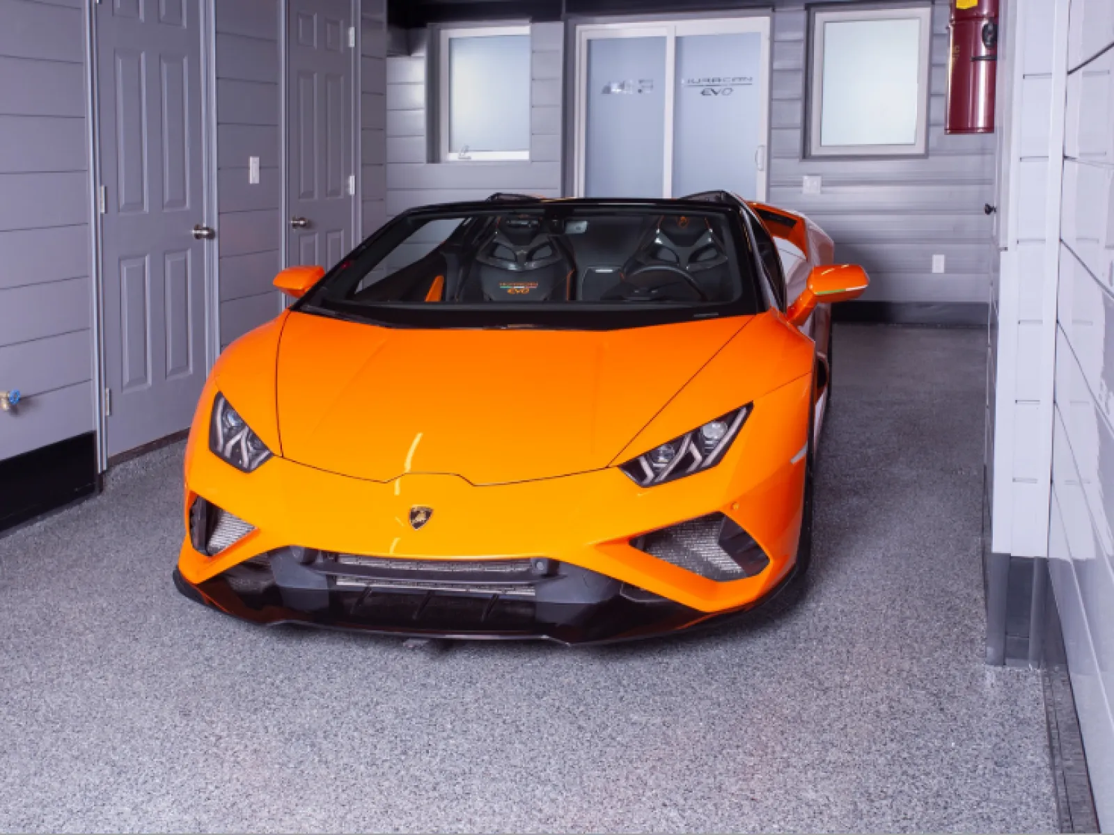 Bright orange Lamborghini Huracan Spyder sports car parked in a modern garage with gray walls.
