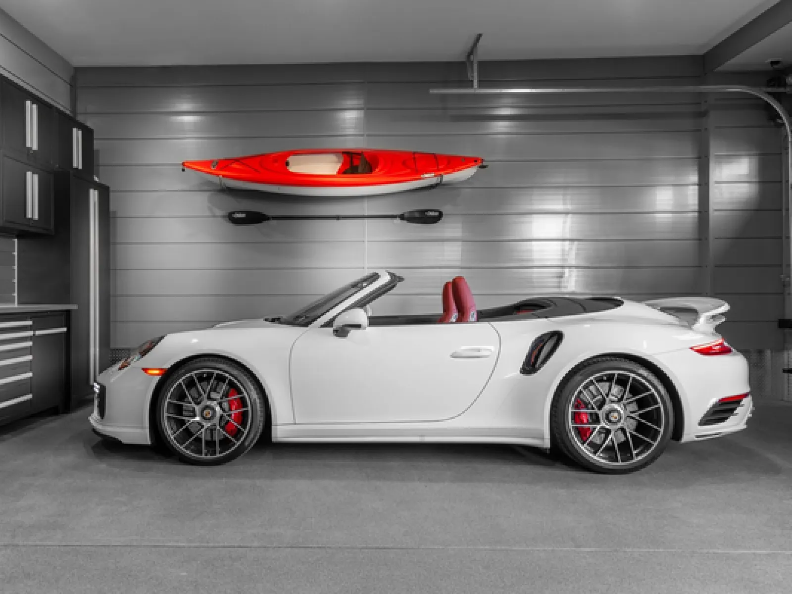 White convertible sports car parked in a sleek modern garage with a red kayak and paddle mounted on the wall.