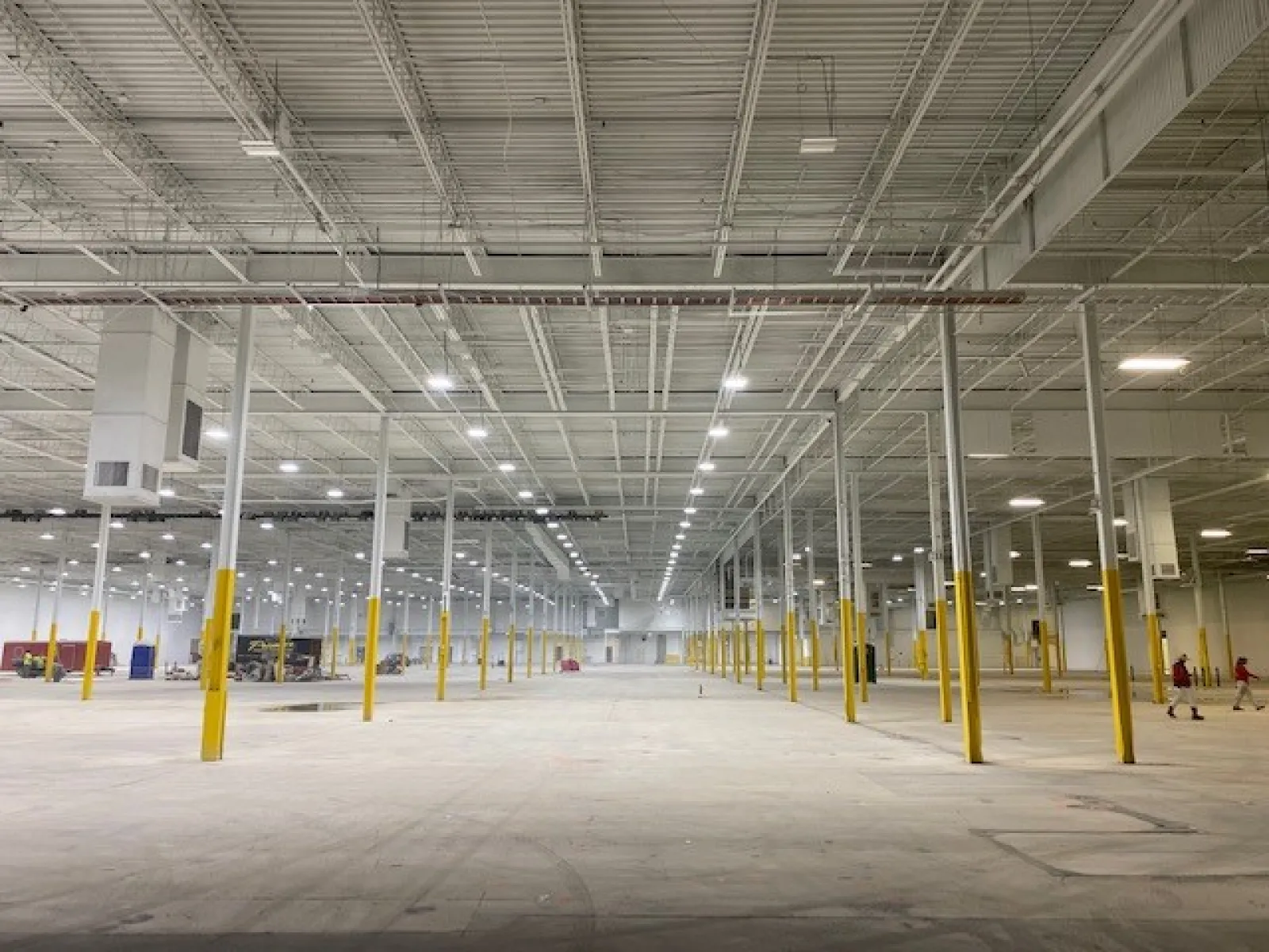 Spacious empty industrial warehouse with numerous yellow poles and bright overhead lighting.