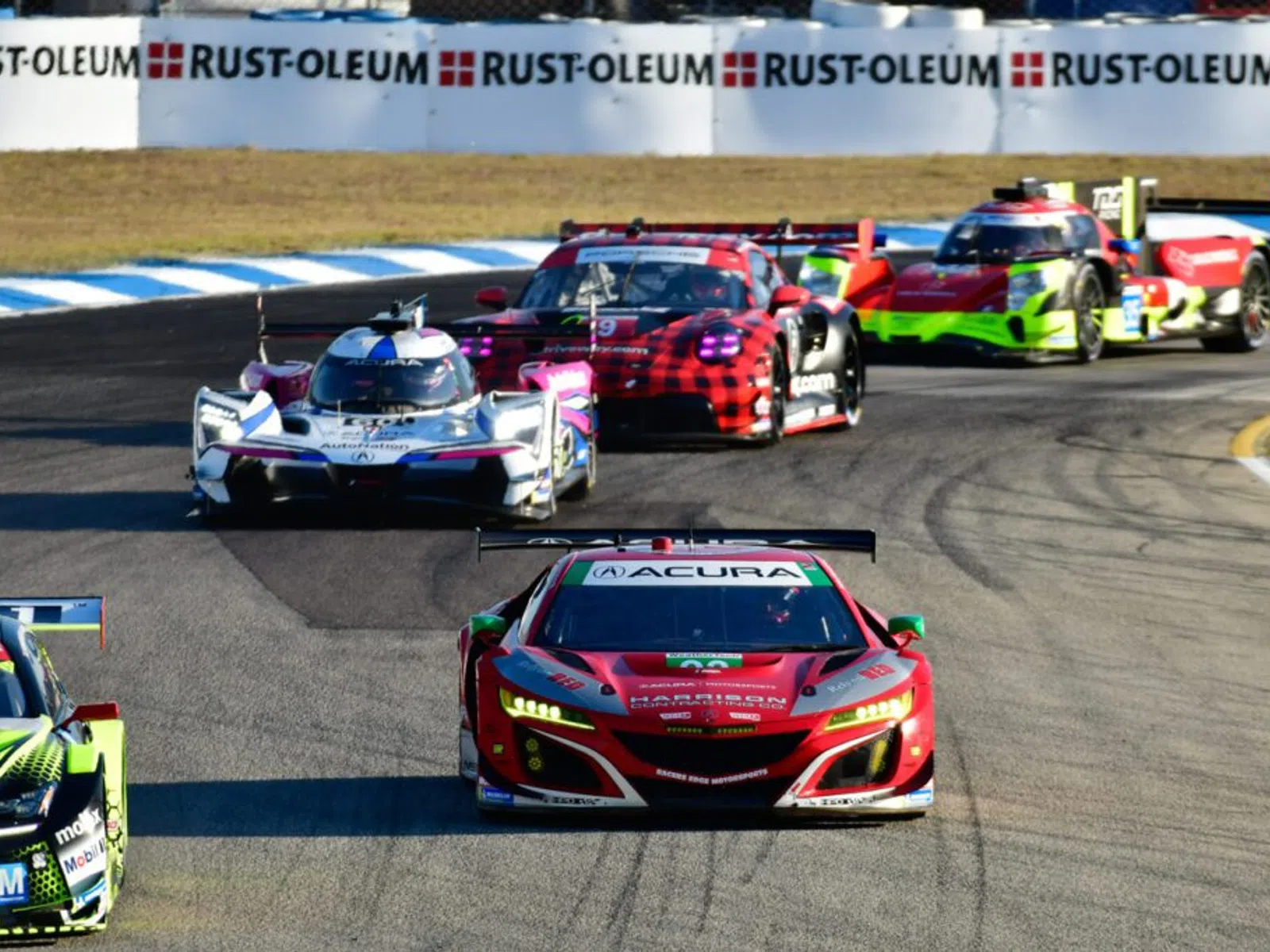 Multiple high-performance race cars competing on a curved race track during a sunny day event.