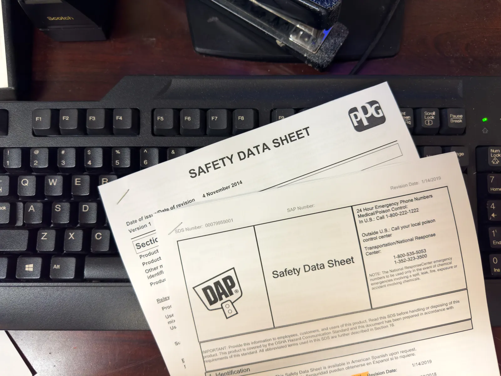 Safety Data Sheet documents lying on a computer keyboard on a wooden desk.