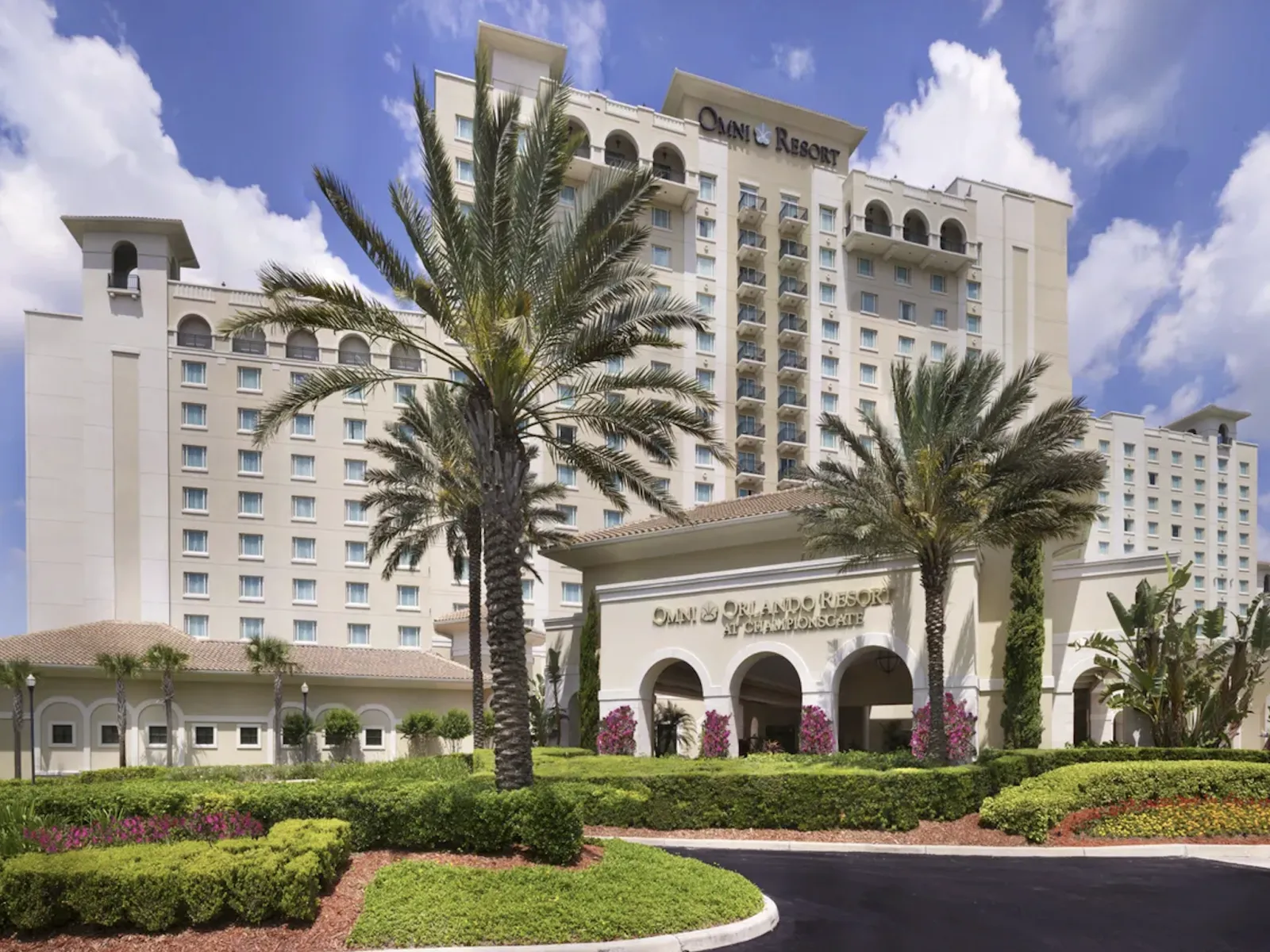 Omni Orlando Resort hotel exterior with palm trees under a partly cloudy blue sky.