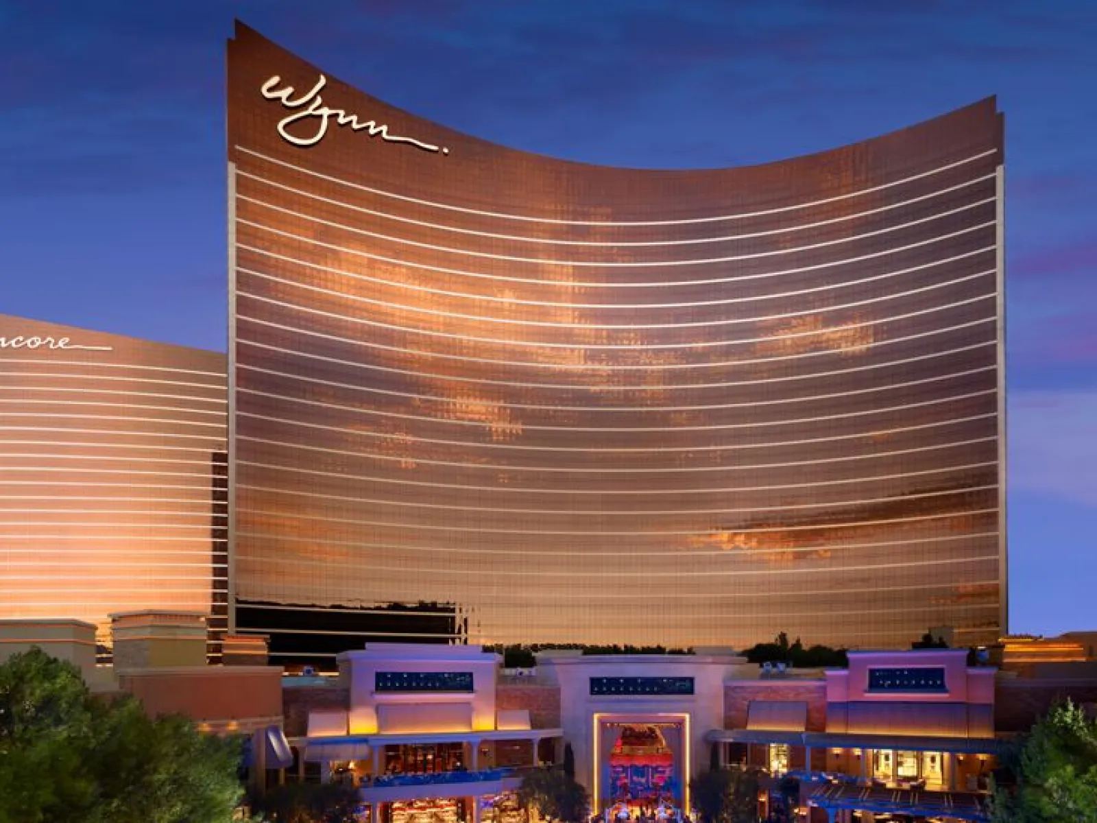 Wynn and Encore hotel towers reflecting sunset colors with illuminated resort entrance at dusk