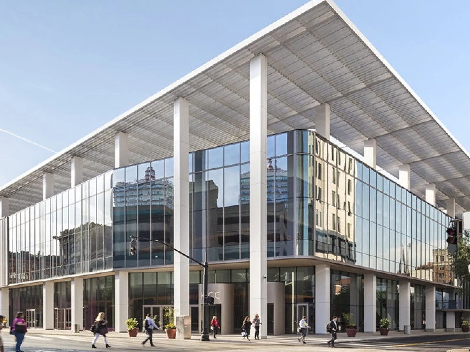 Modern glass office building with large white columns and people walking on the street in daytime urban setting