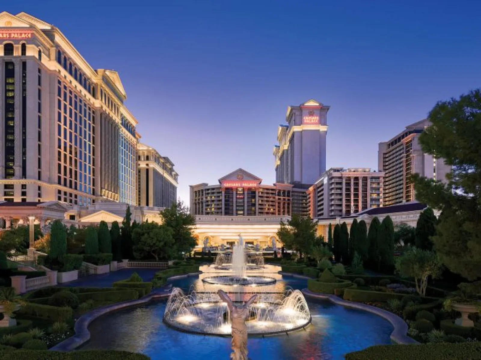 Caesars Palace hotel and casino with illuminated fountains and gardens at dusk in Las Vegas.