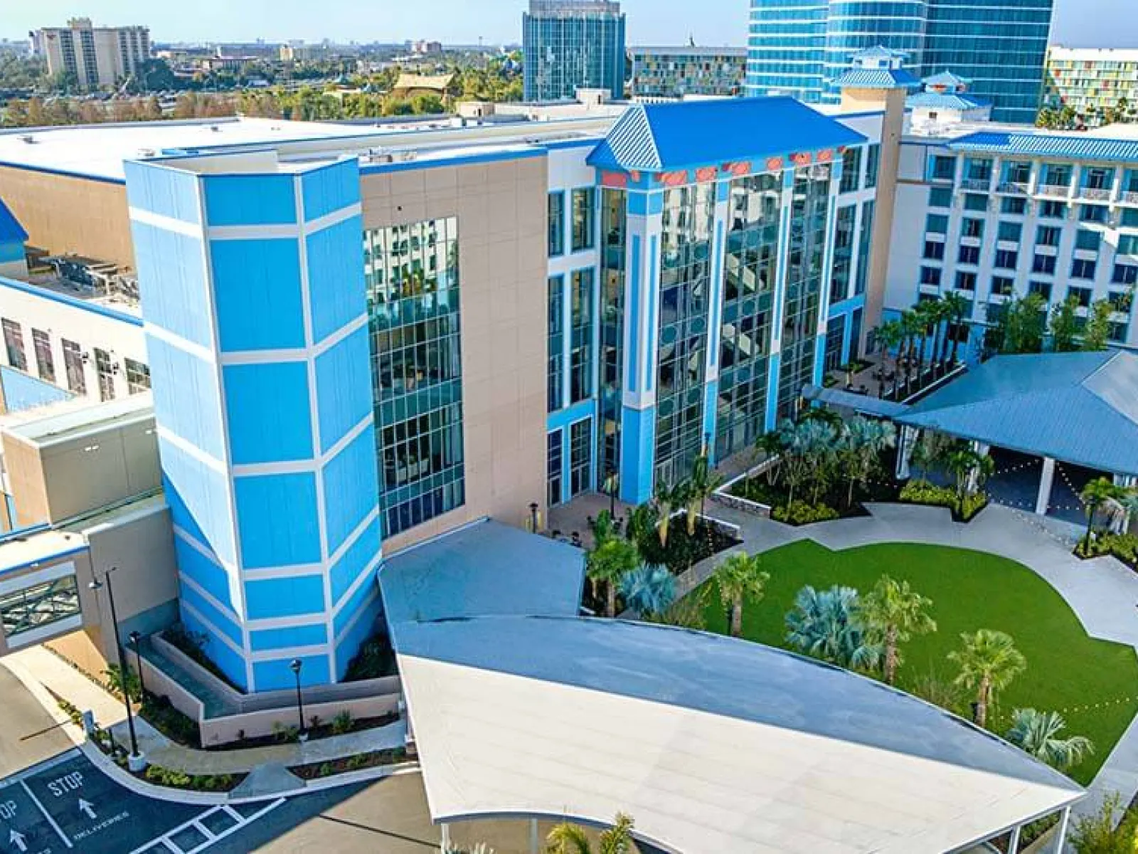 Aerial view of a modern blue and beige office complex with green spaces and surrounding cityscape under clear sky
