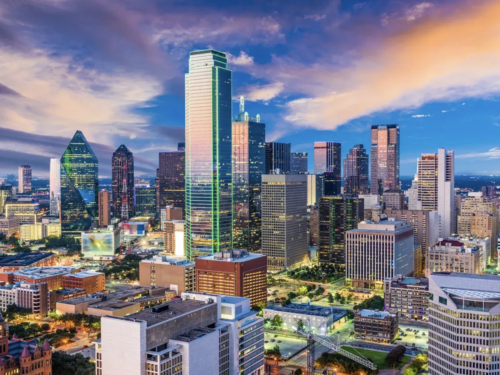Dallas city skyline at sunset with illuminated skyscrapers and colorful sky.