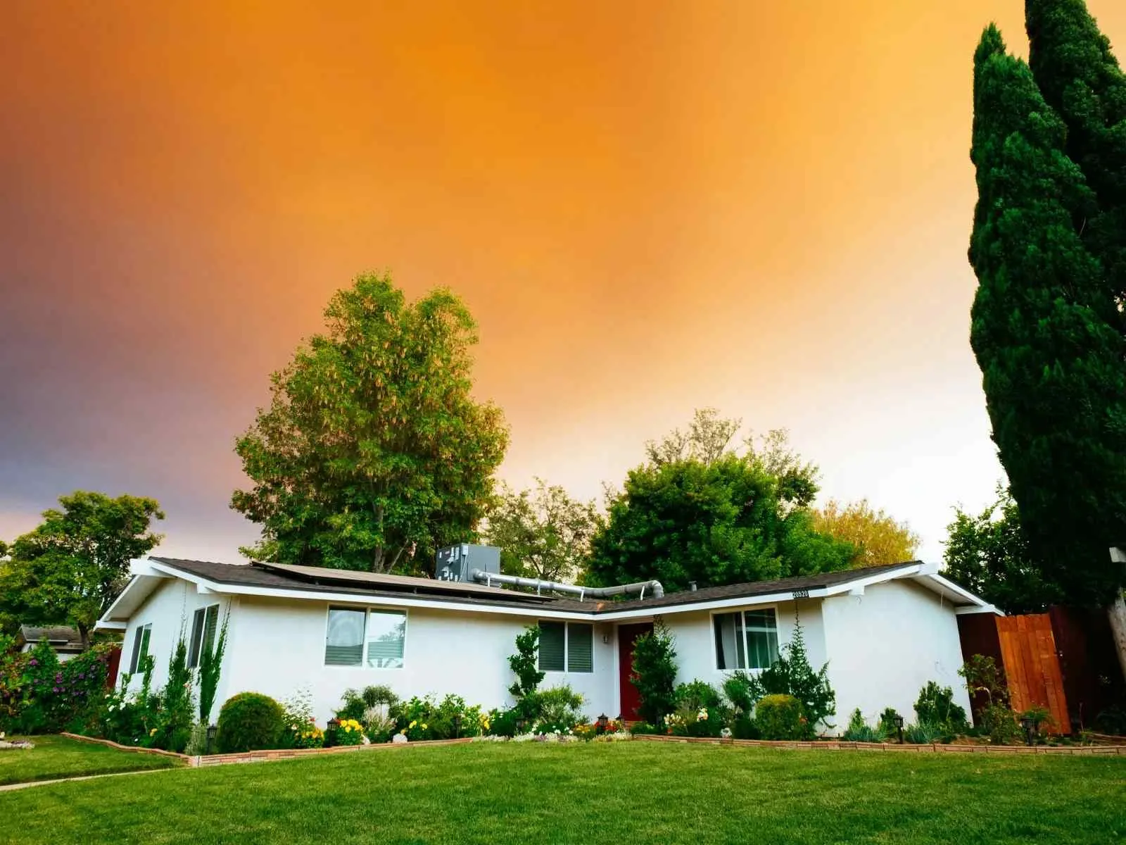 Single-story white house with green lawn and vibrant trees under an orange sunset sky.