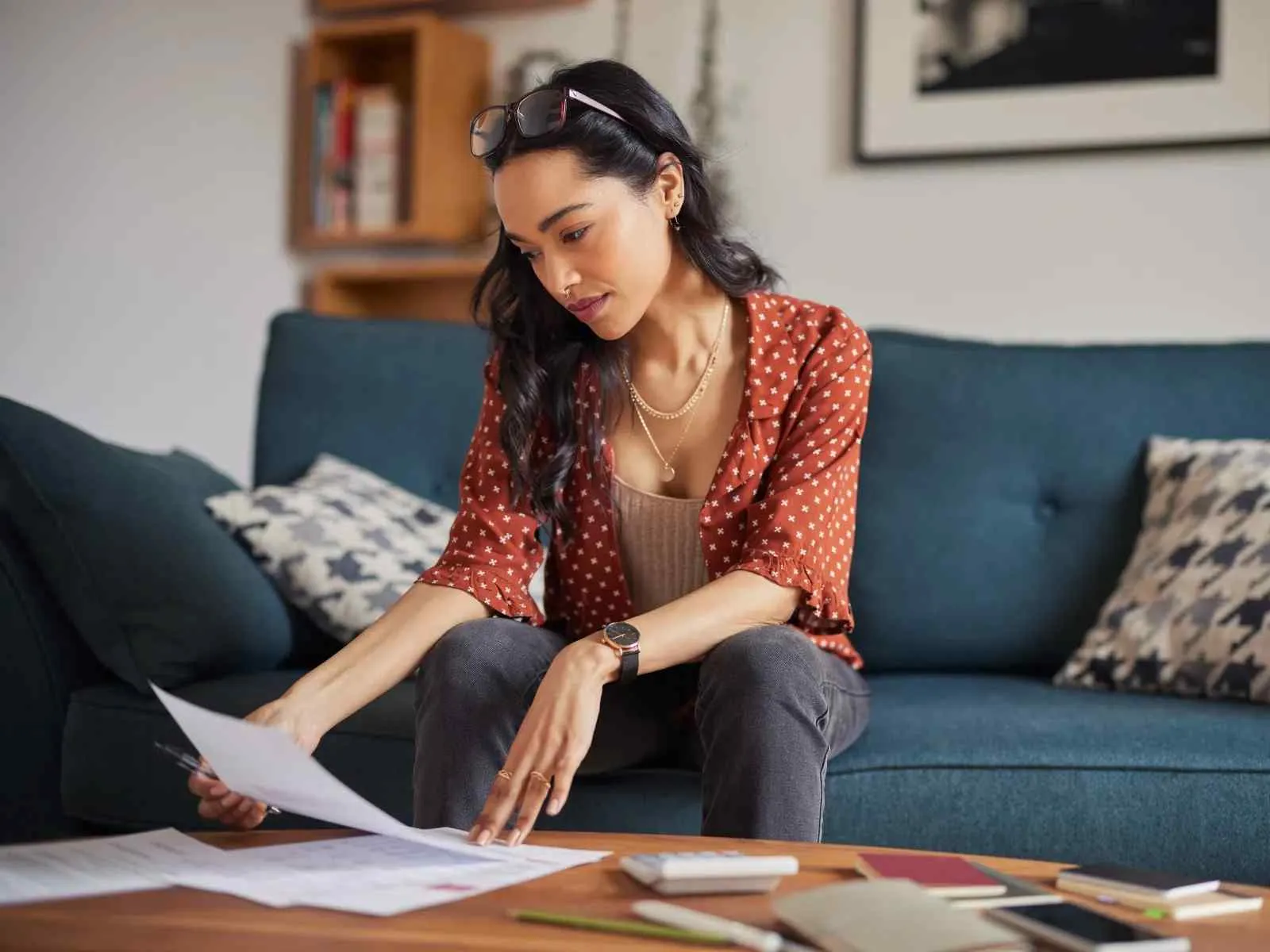 Woman sitting on a blue couch reviewing papers on a wooden table in a cozy living room.