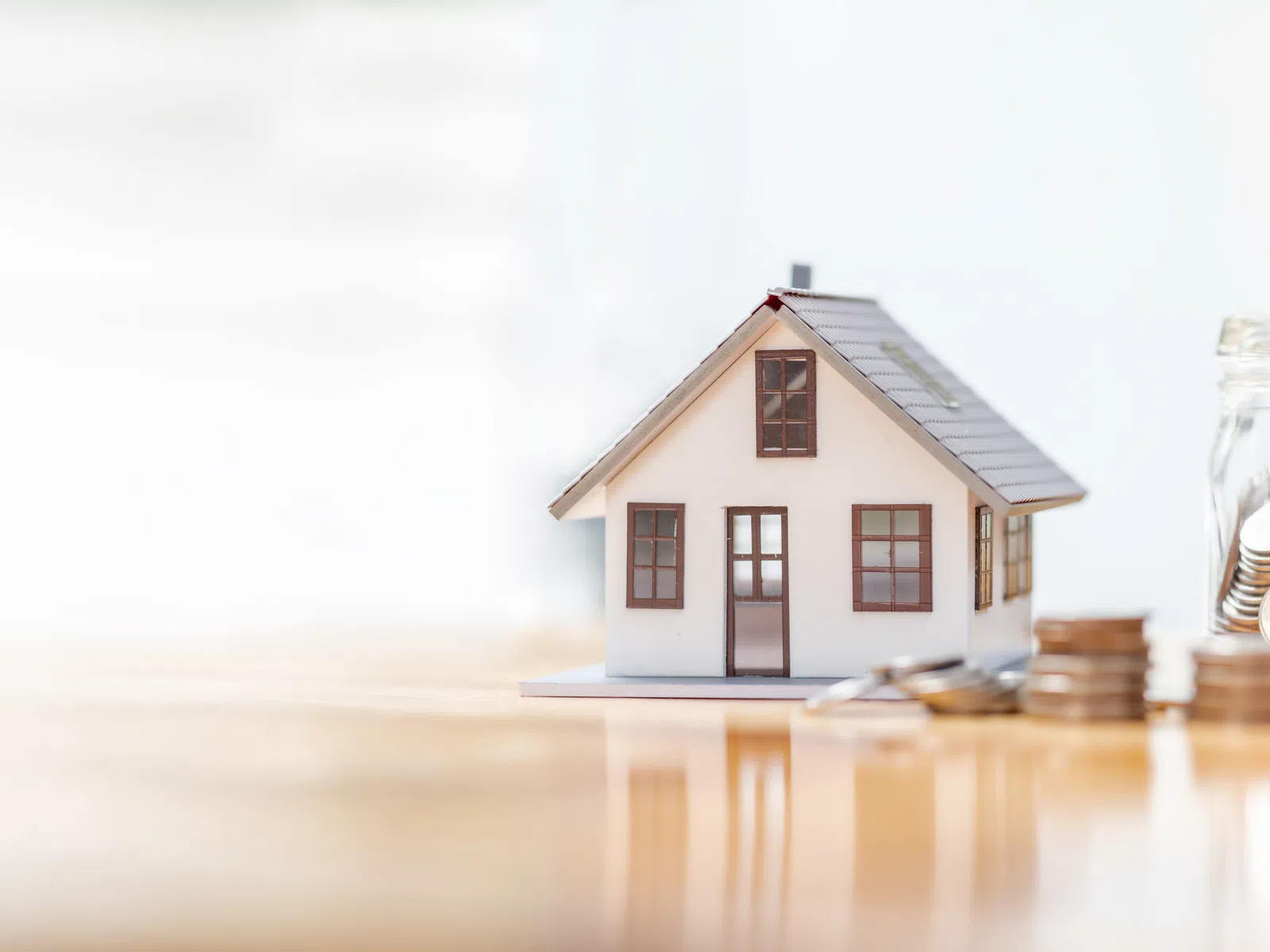 Miniature house model with stacked coins and a jar full of coins, symbolizing home savings or mortgage investment.