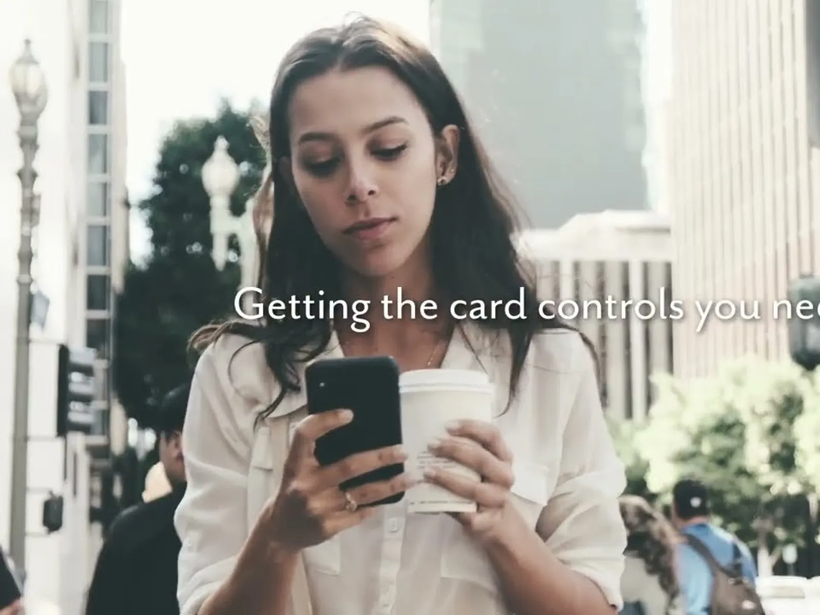 Woman in urban setting holding coffee and smartphone with text about card controls overlaid.
