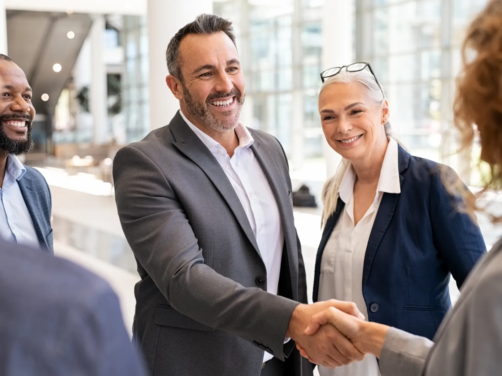 Business professionals smiling and shaking hands in a modern office setting during a meeting.