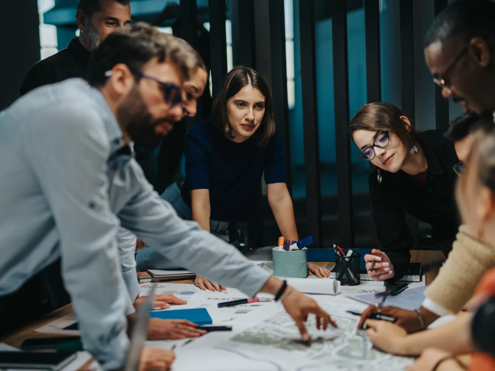 Team of professionals collaborating over blueprints and documents during a focused office meeting.