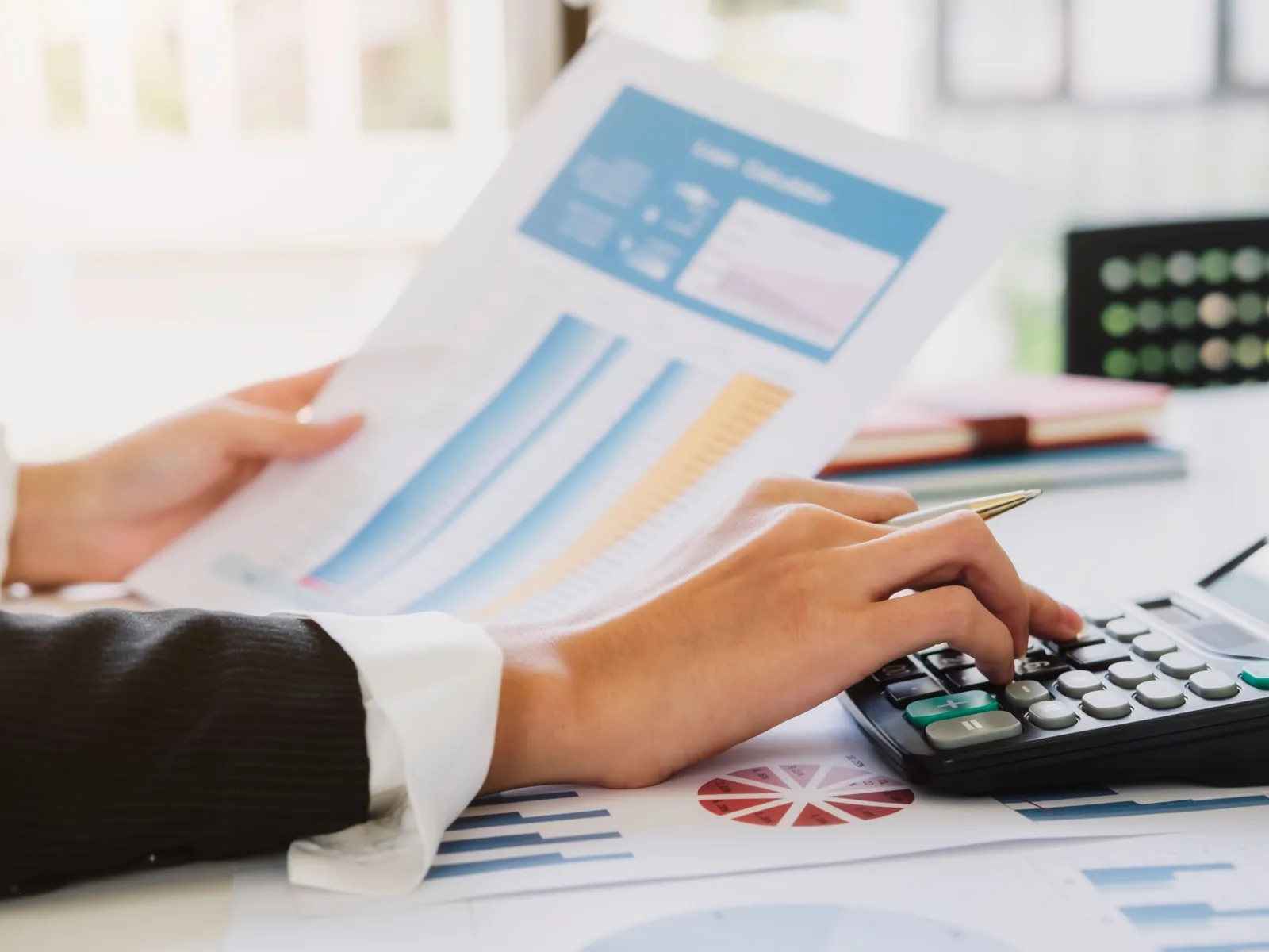 Person analyzing charts and graphs while using a calculator to review financial data and reports.