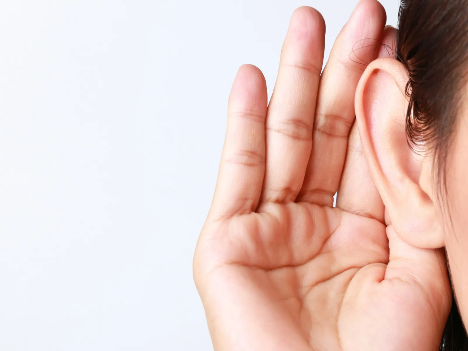 Close-up of a person cupping their hand behind their ear to hear better on a white background.