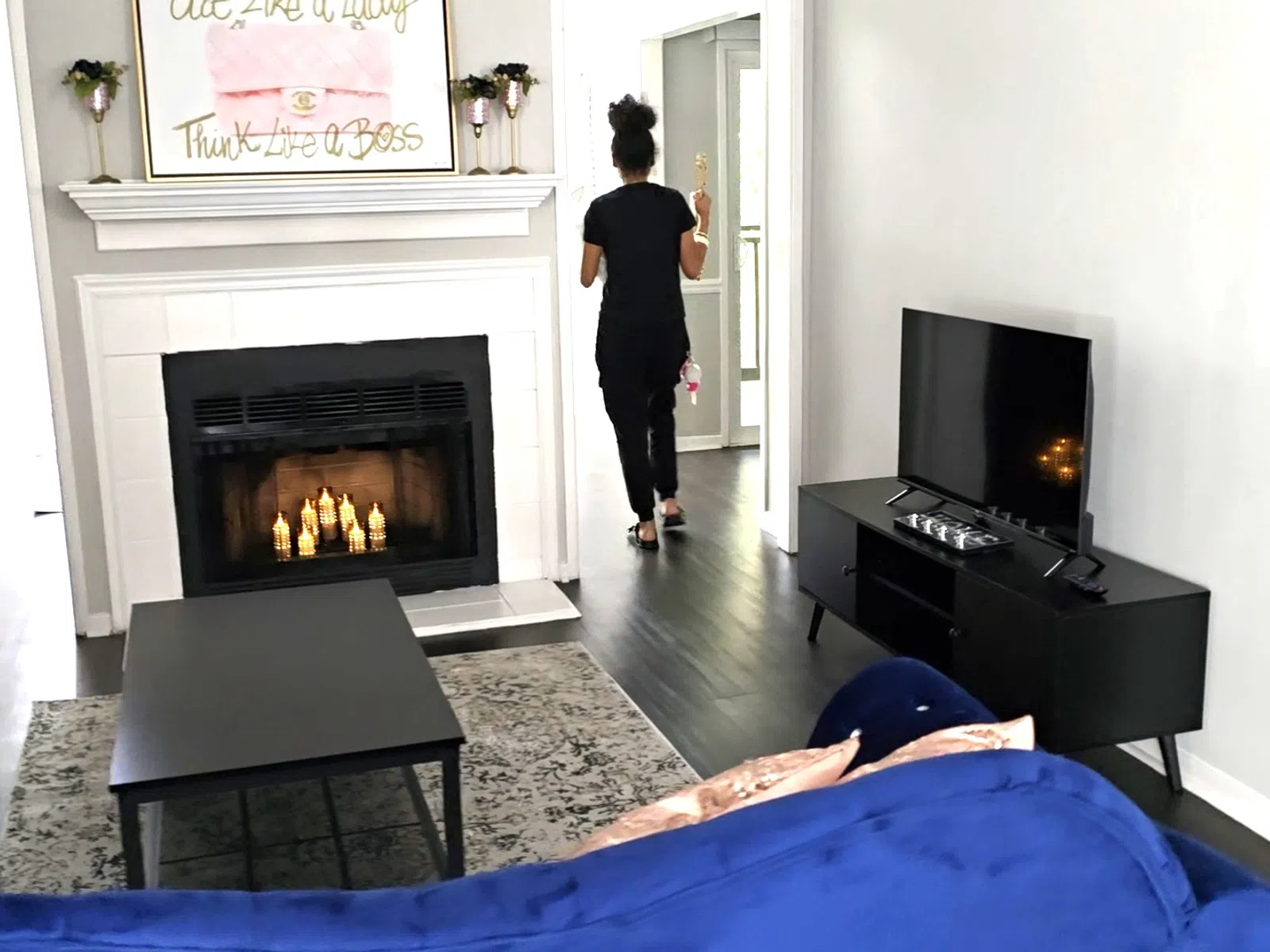 Modern living room with blue velvet sofas, black coffee table, fireplace, and TV console, person walking away.