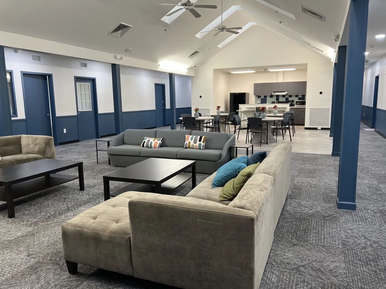 Spacious lounge area with sofas, pillows, coffee tables, dining area, and high vaulted ceiling with fans.
