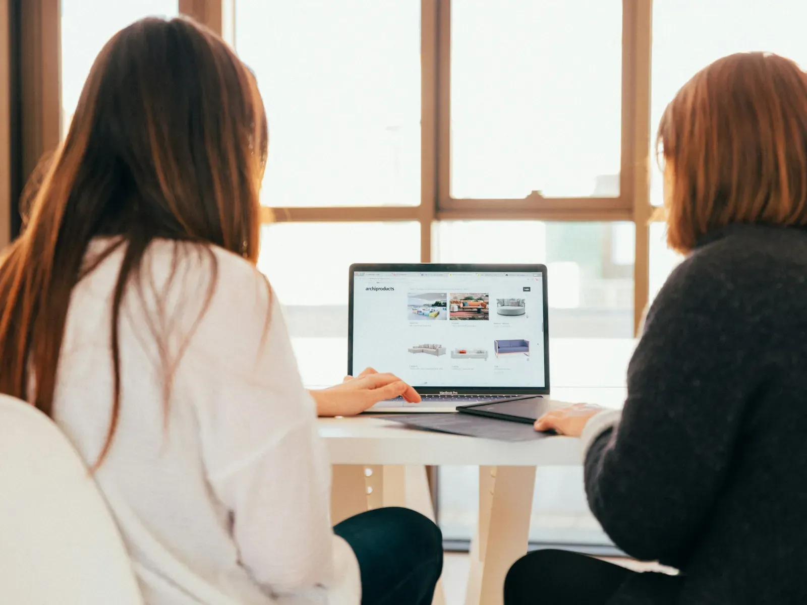 Two colleagues smiling and discussing work while looking at a laptop in a modern office-space with brick wall.