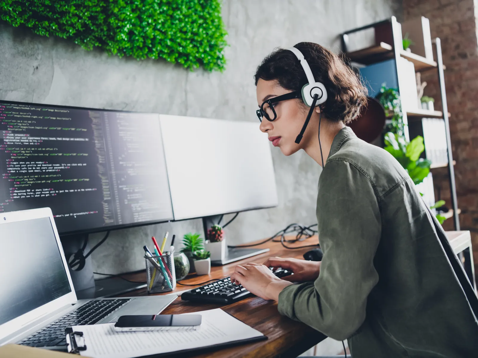 Focused woman wearing headset programming on desktop with multiple monitors in modern office workspace