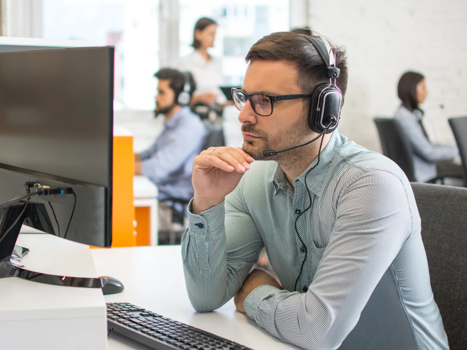 Focused customer service representative wearing headset working at computer in busy office environment