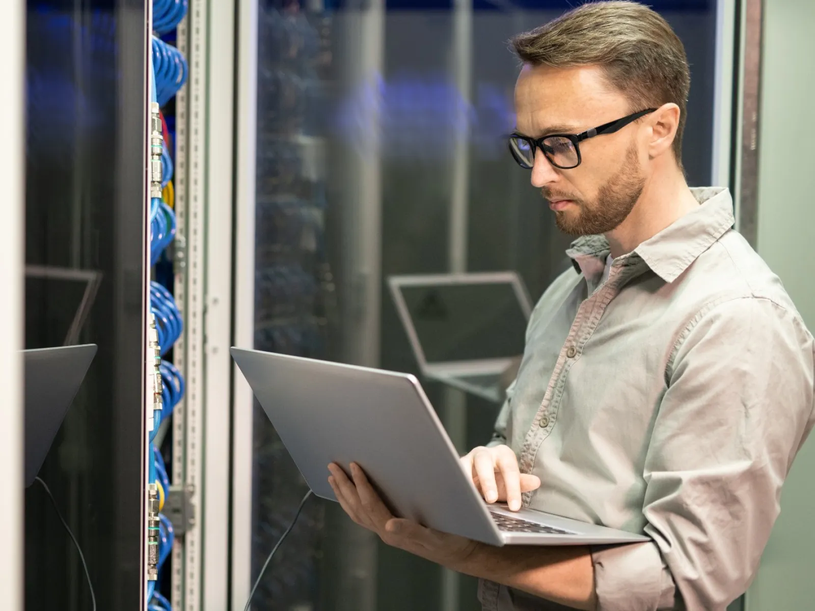 IT technician working on a laptop inside a server room with network cables and server racks.