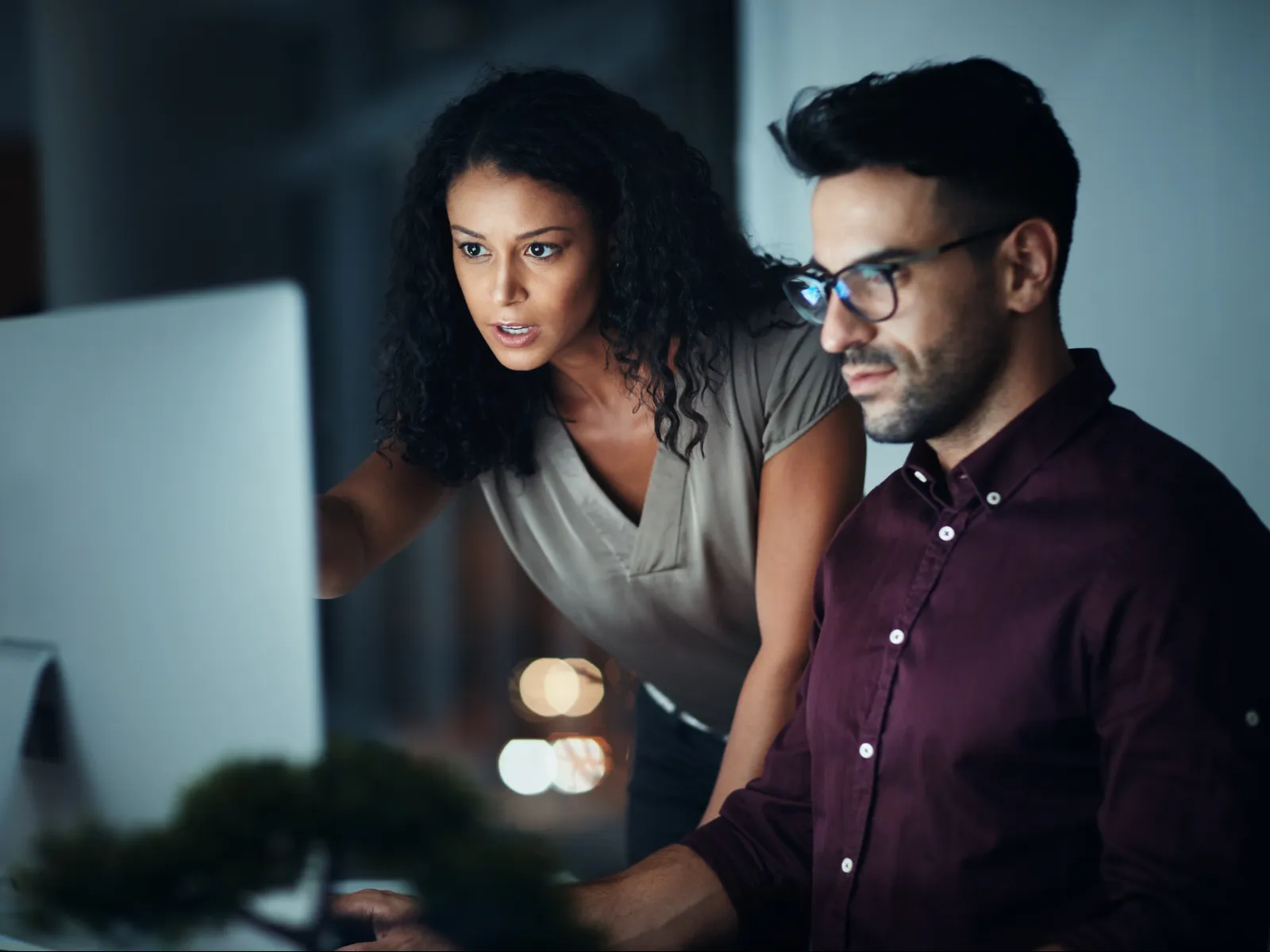 Two focused professionals collaborating and working on a desktop computer in a modern office environment.